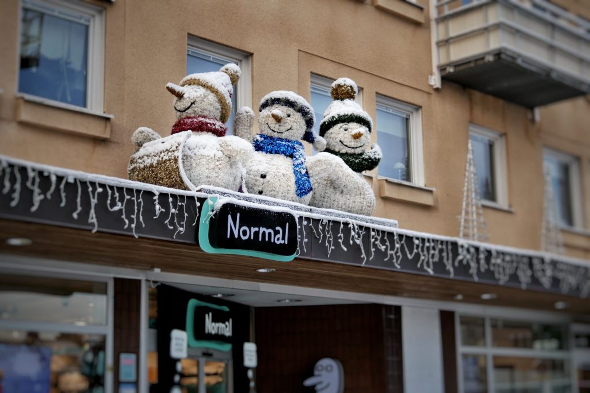 Snowmen decoration standing on the top of a shop sign - Normal.