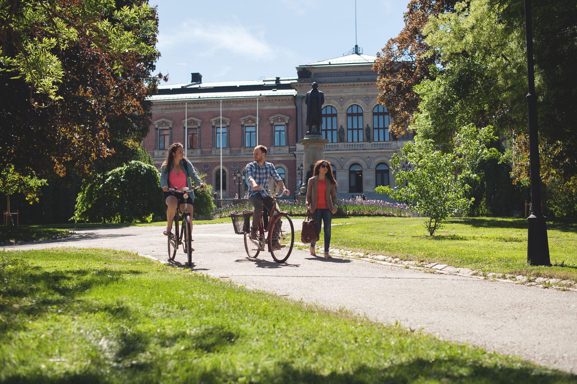 A man and a woman bike past a pedestrian woman at the Uppsala Univerity campus.