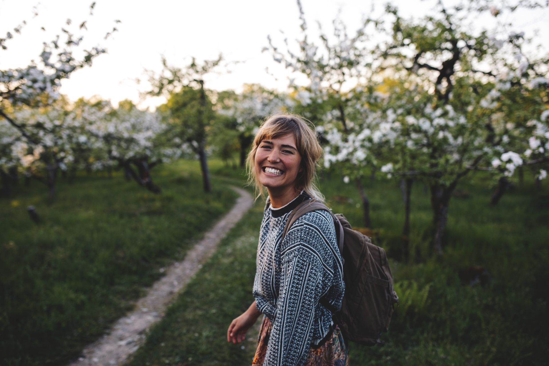 A woman smiling to the camera among blooming apple trees.