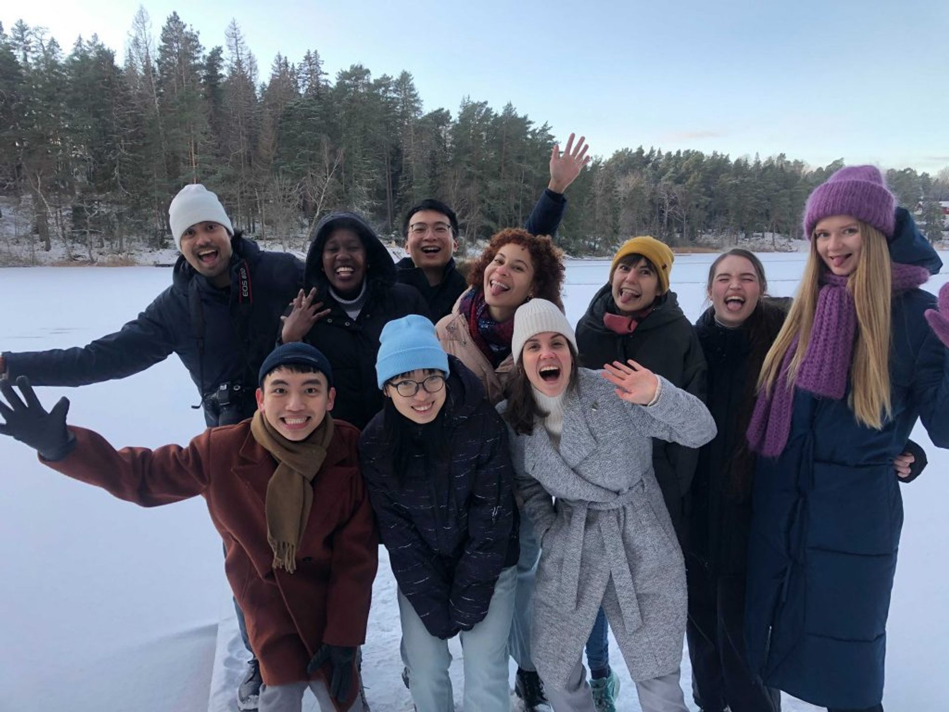 A group of people laughing and posing for a photo in front of a frozen lake. 