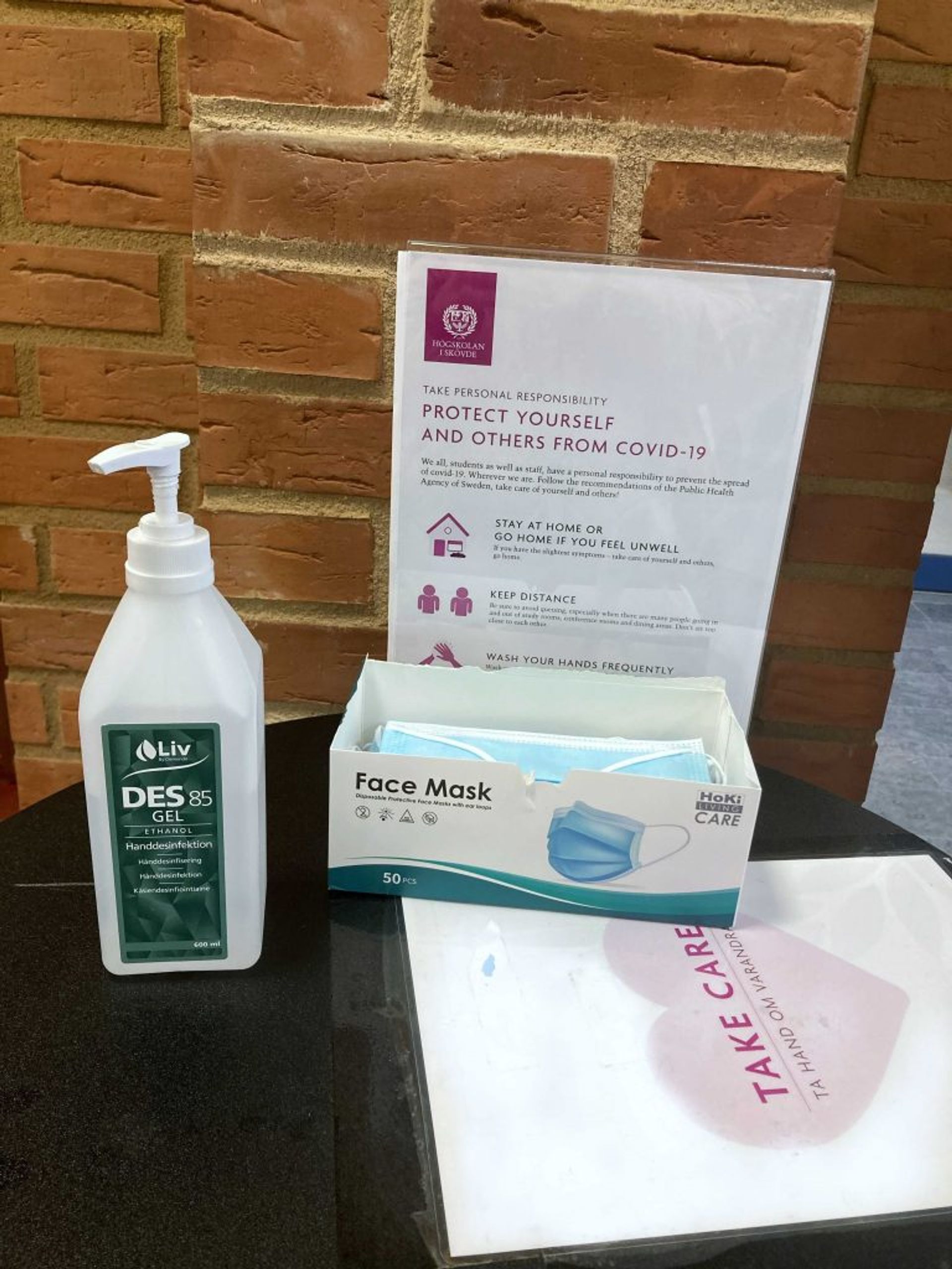 A small table with desinfectant, free face masks, and a sign that recommends to protect yourself and others from COVID-19.