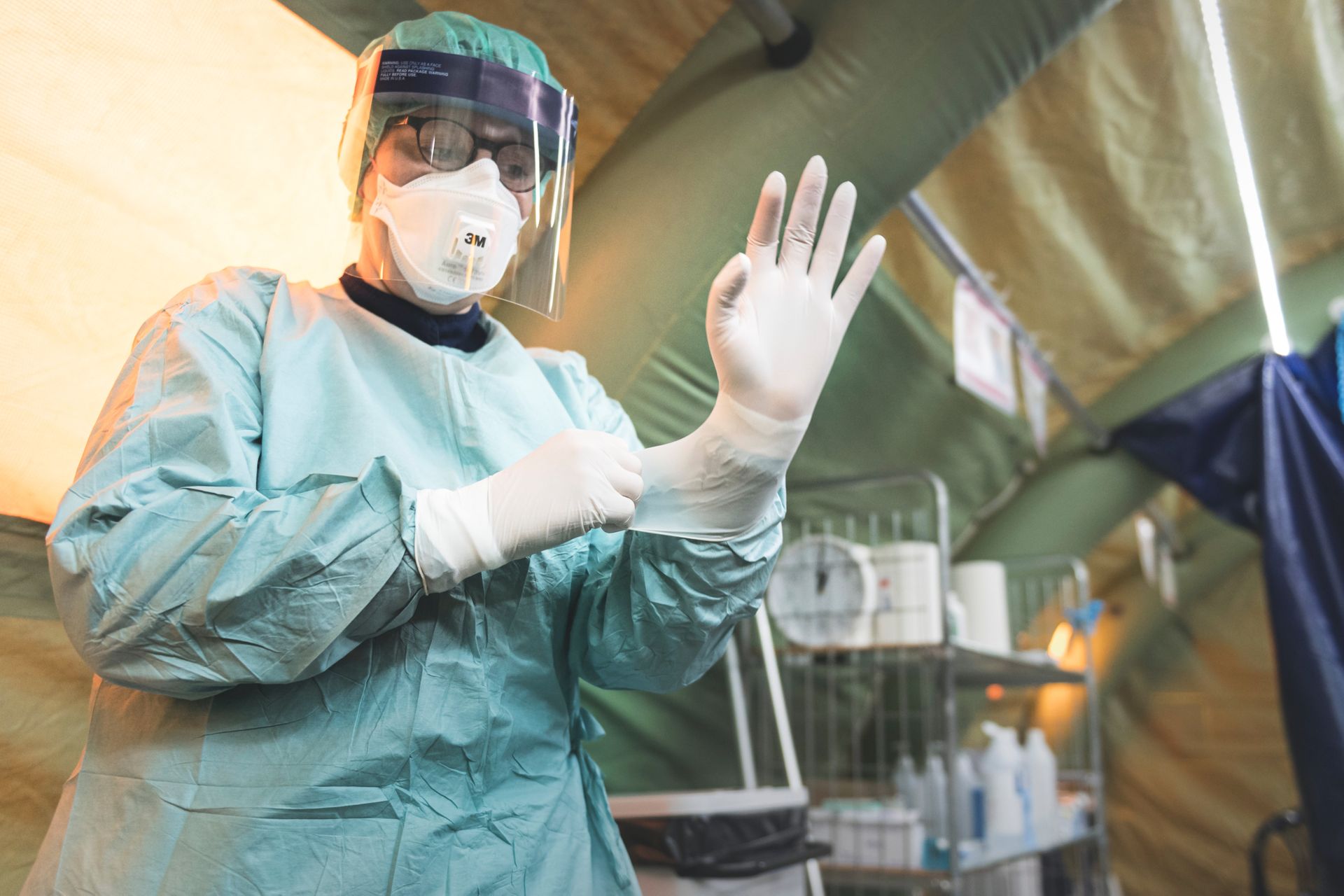 A healthcare worker is putting on personal protective equipment inside a tent.