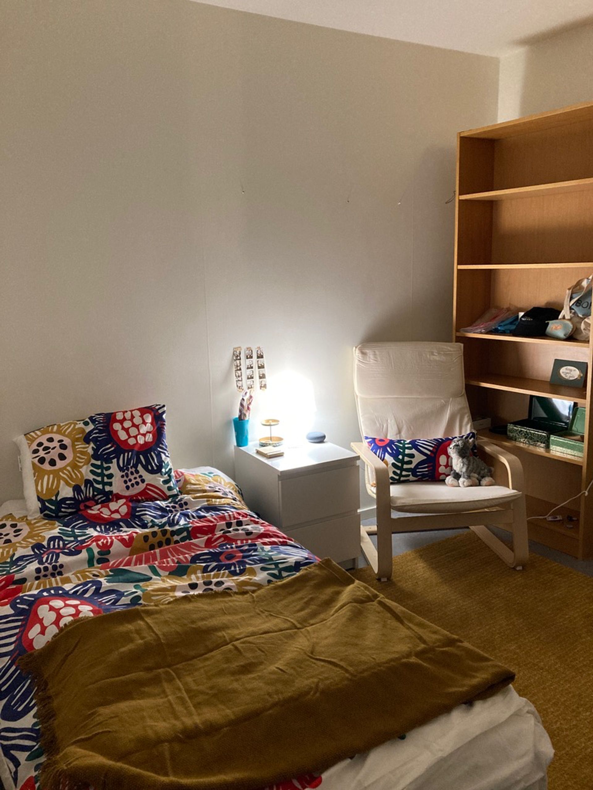 An accommodation witb a bed, chair, and bookshelf in a small bedroom.