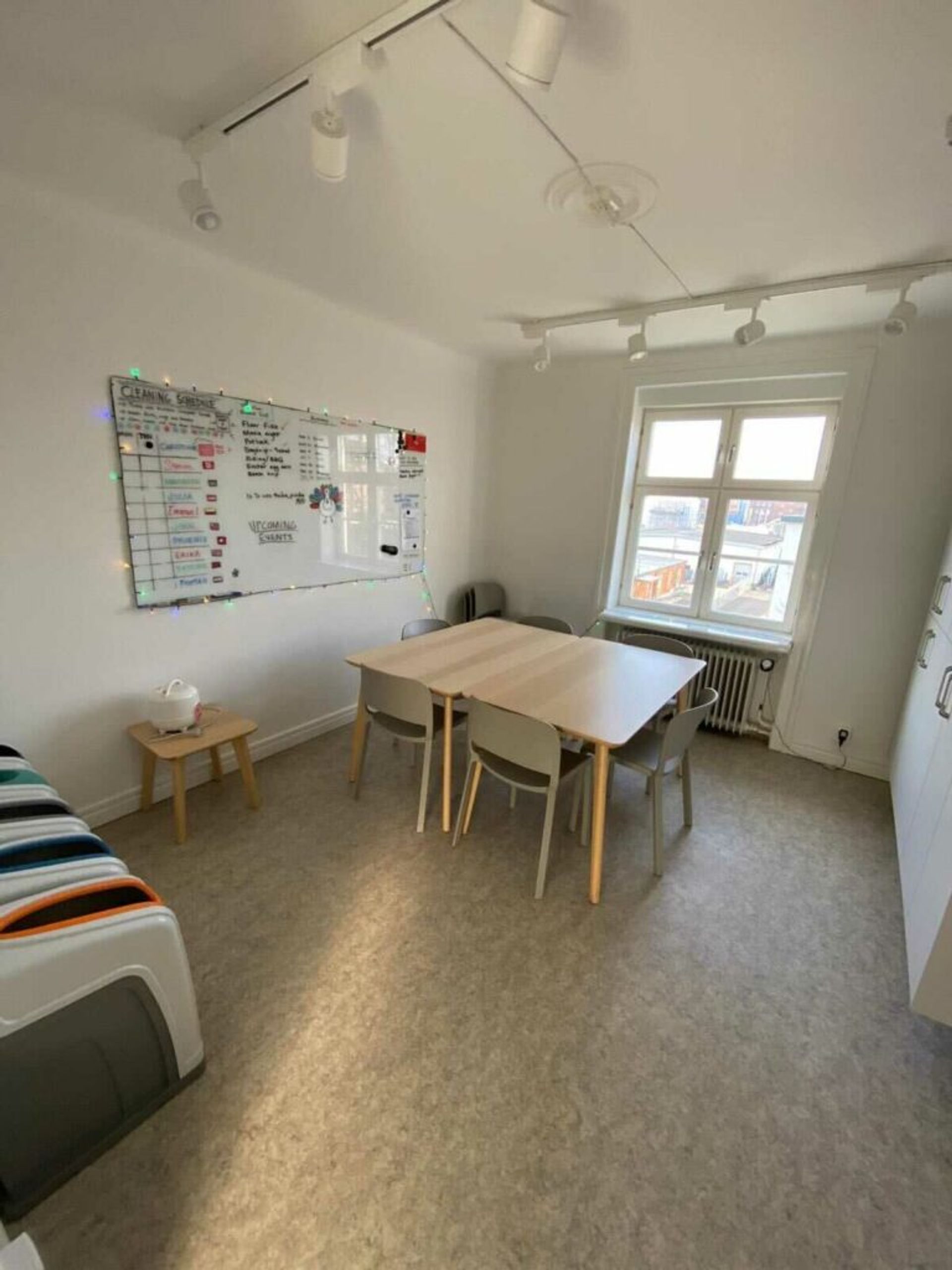 A room with a white board and a table with four chairs in a shared accommodation. 