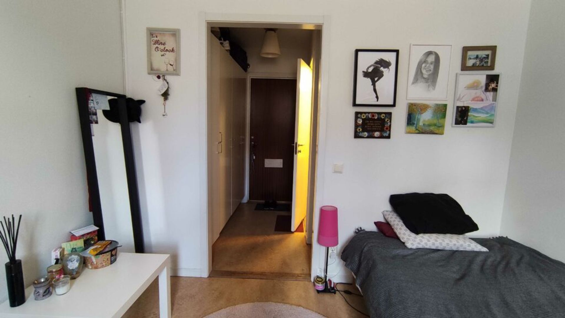 An entrance to an accommodation with pictures, bed and a mirror. 
