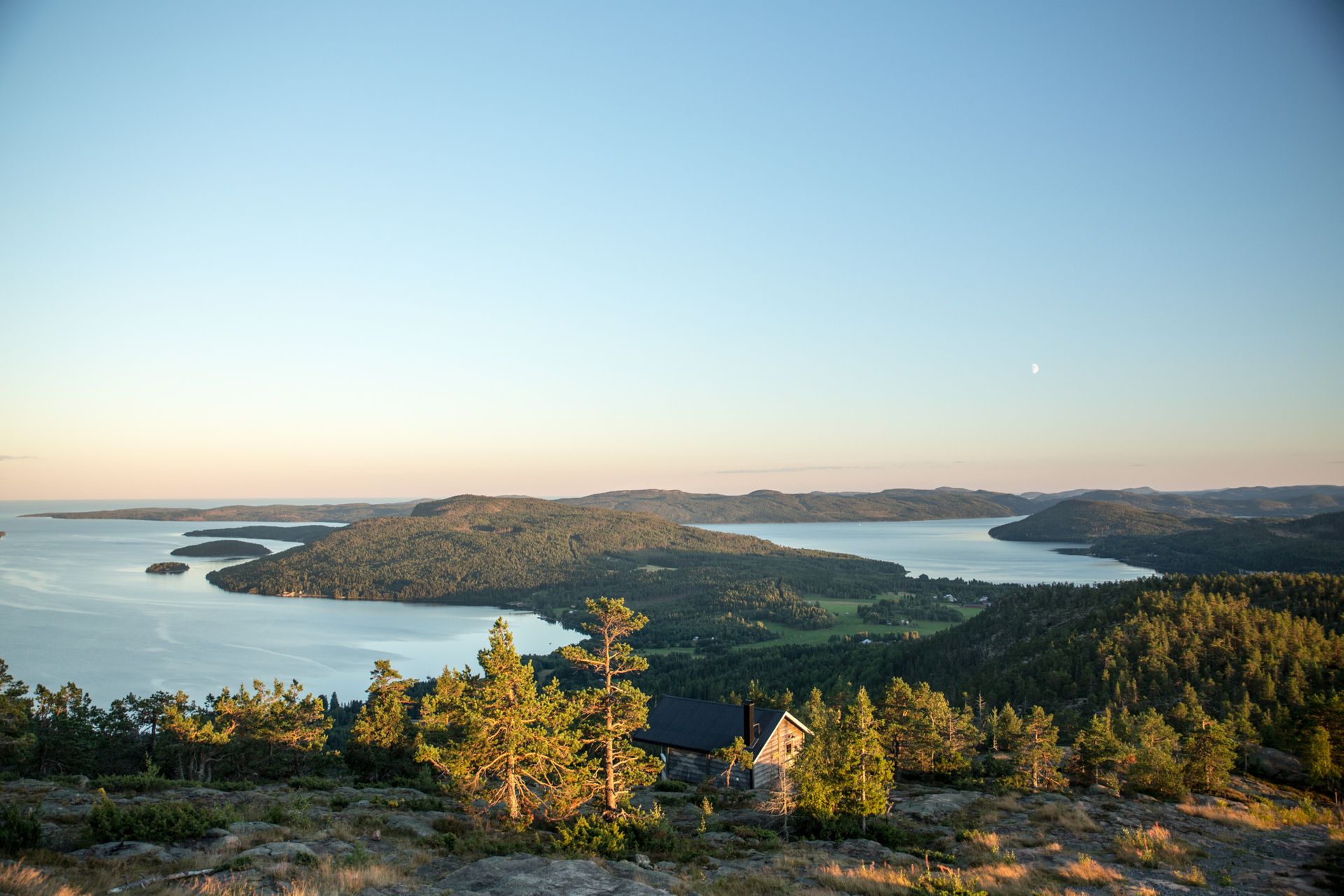 A scenic view of the forest-rich High Coast landscape reaching into the ocean with a cabin the foreground.