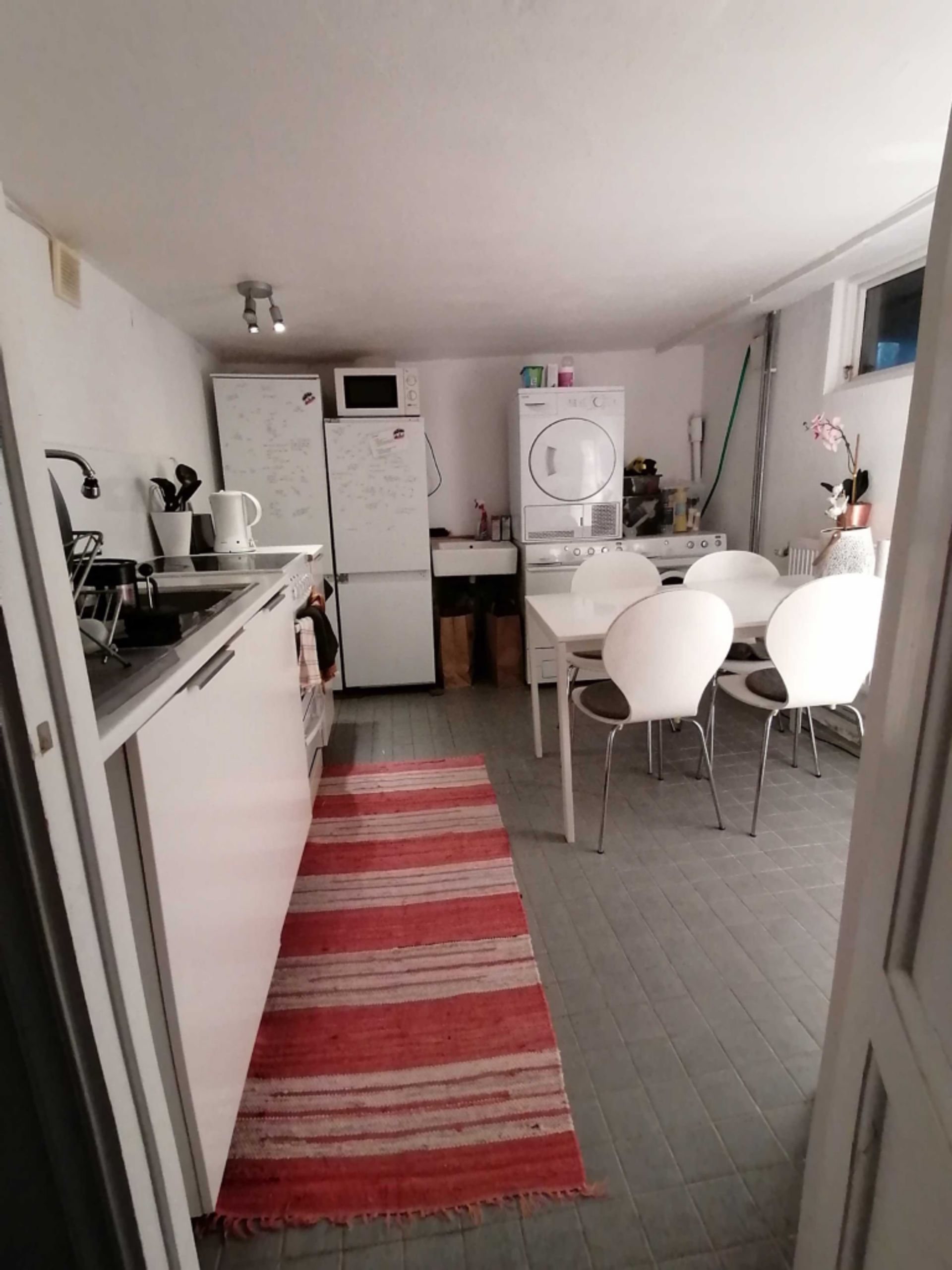 White kitchen with a fridge, washing machine and a dryer. It also includes a table with four chairs.  