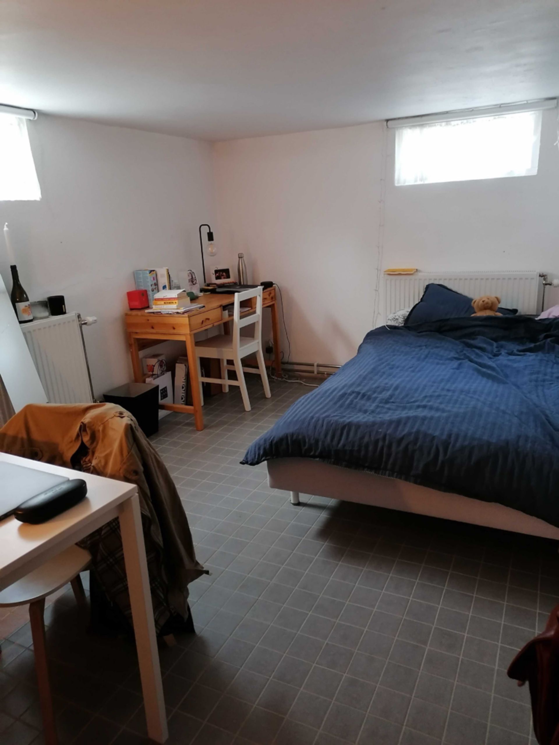 An accommodation in the basement with double bed, desk and a chair. 