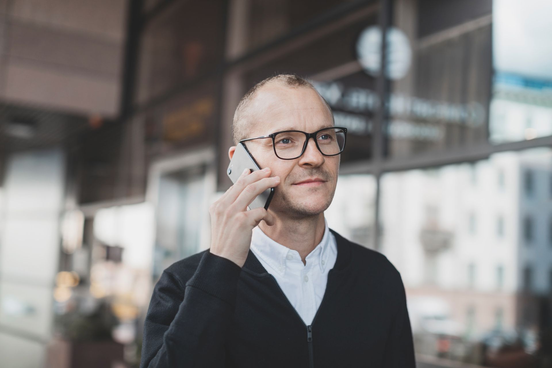 A man stands outside on a city street, holding a phone up to his ear.