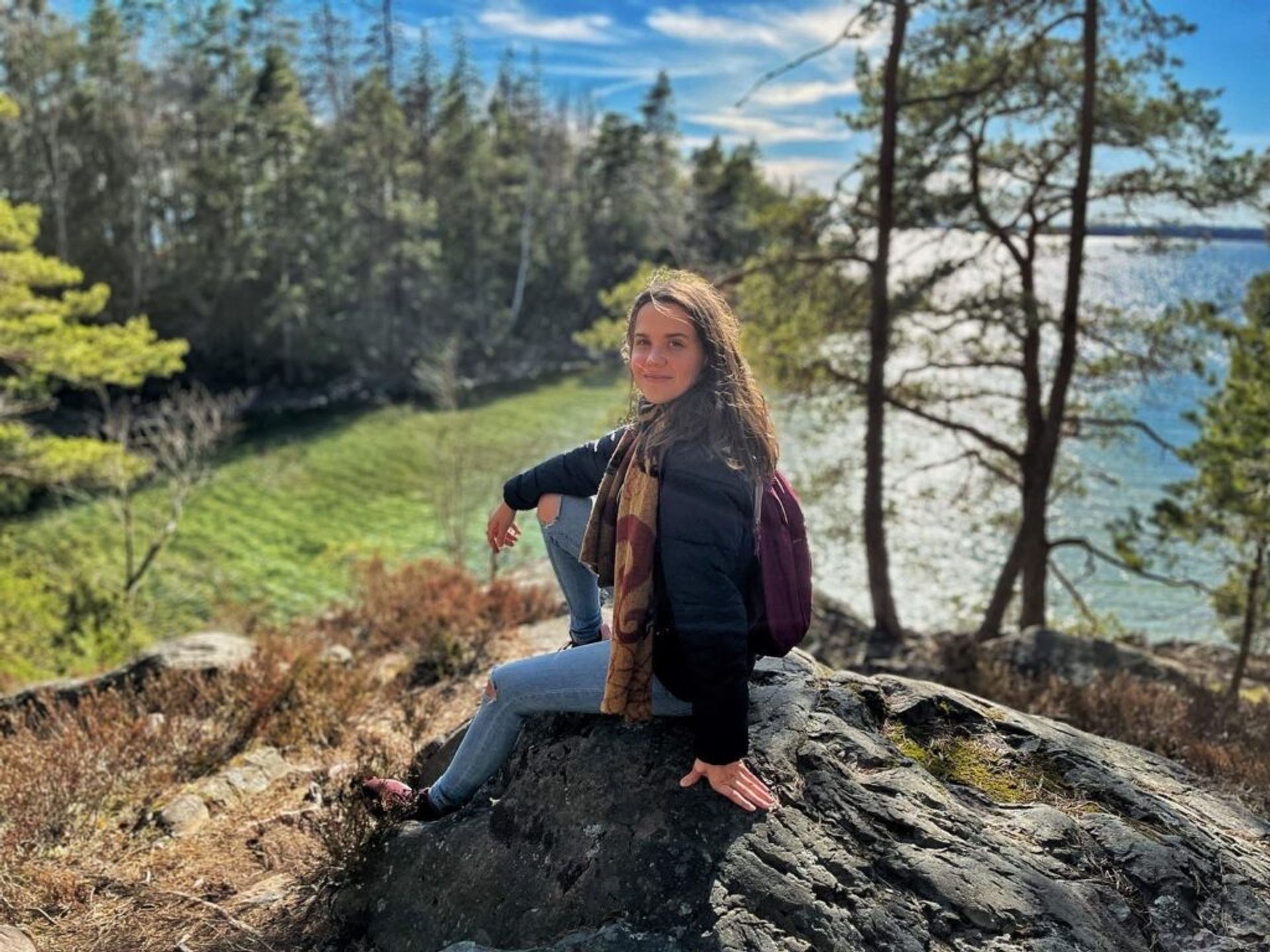 Woman sitting on a rock in a forest with a lake in the background.