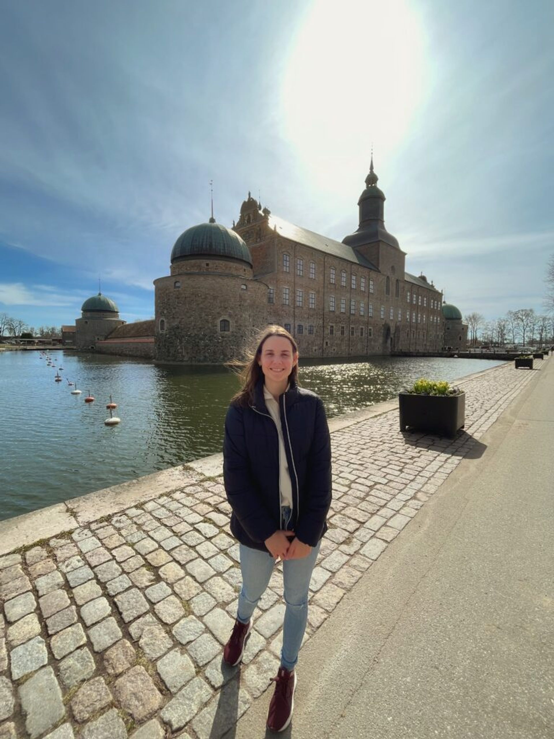 A woman smiles in front of a castle surrounded by water.