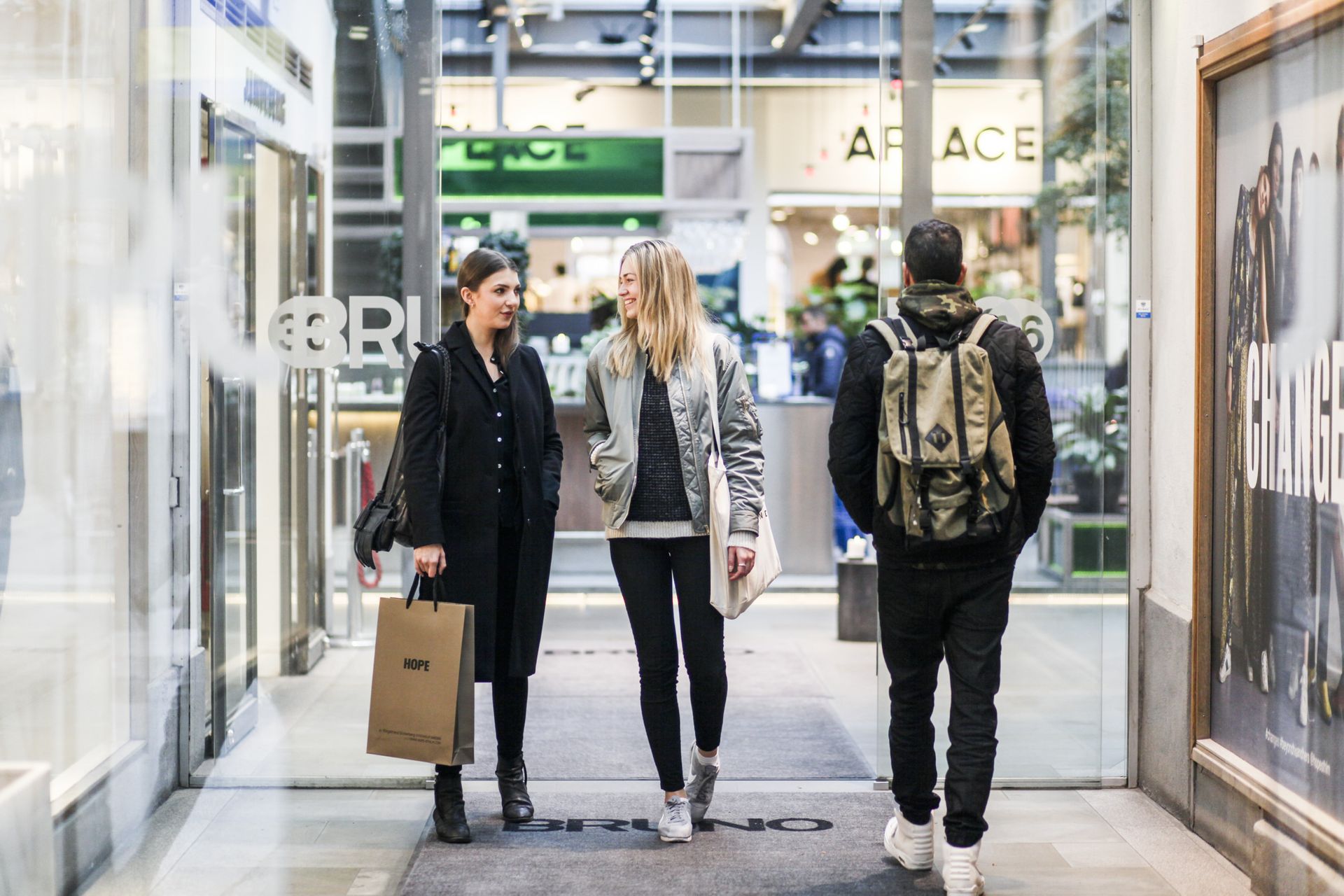 A man with a backpack exits a store in Stockholm as two women enter it.