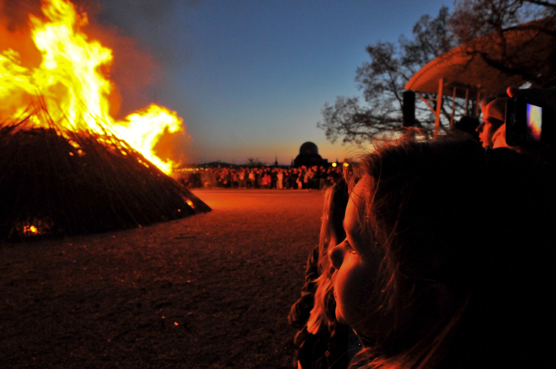Crowds of people stand in the dark looking at a bonfire.