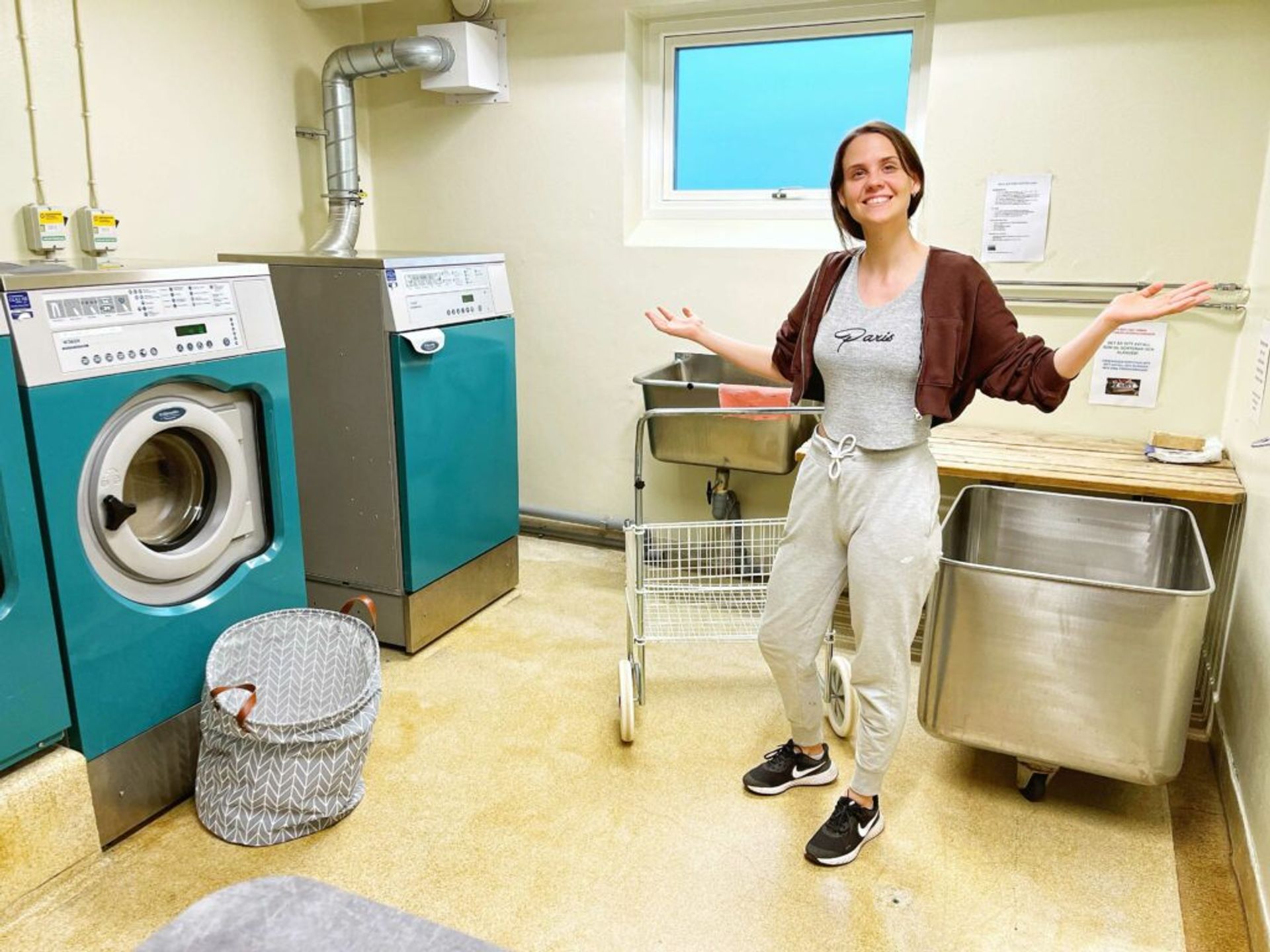 A girl standing in the middle of a room with two washing machines and dryer. 
