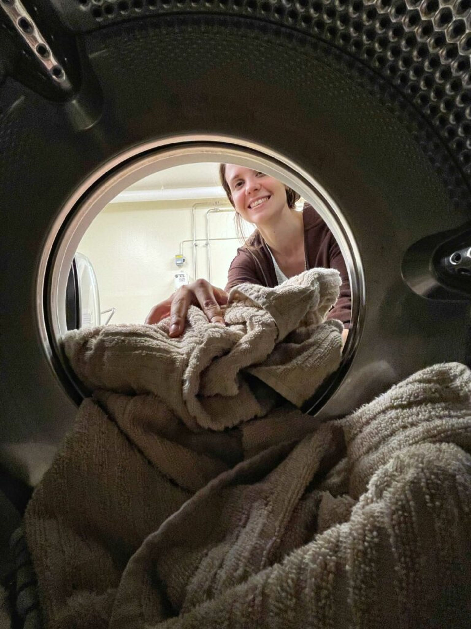 A photo taken from the inside of a washing machine when a girl is putting a towel into the washing machine.  