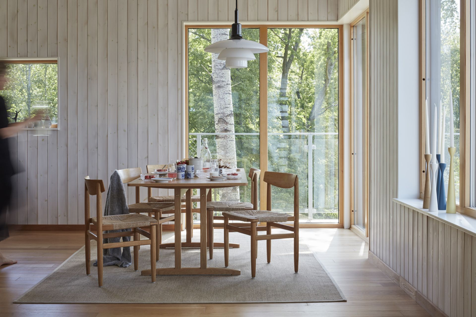 A bright dining room with large windows, with chairs made of wood and reed, and a wooden table where breakfast is served.