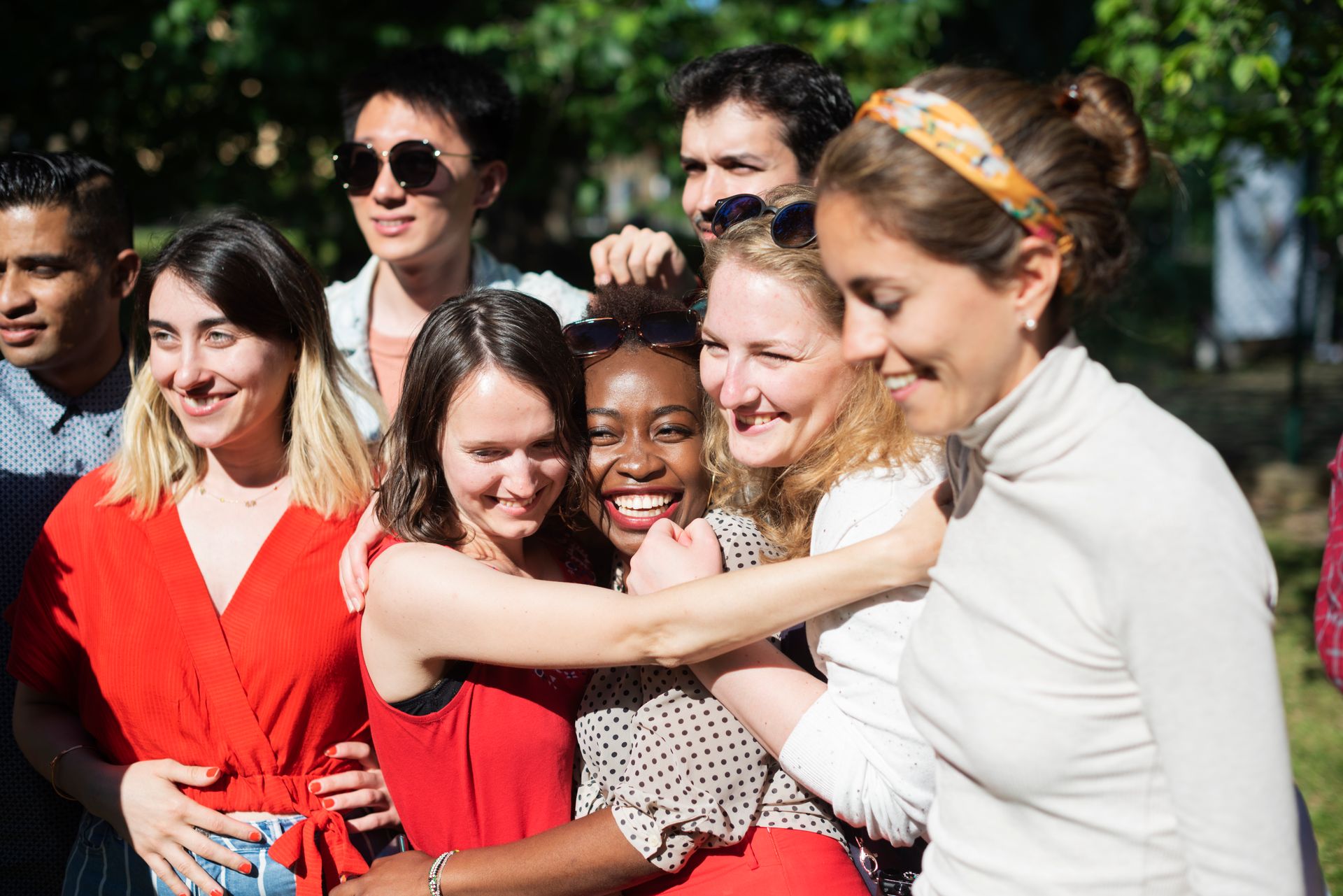 A group of friends in a park are embracing, smiling.