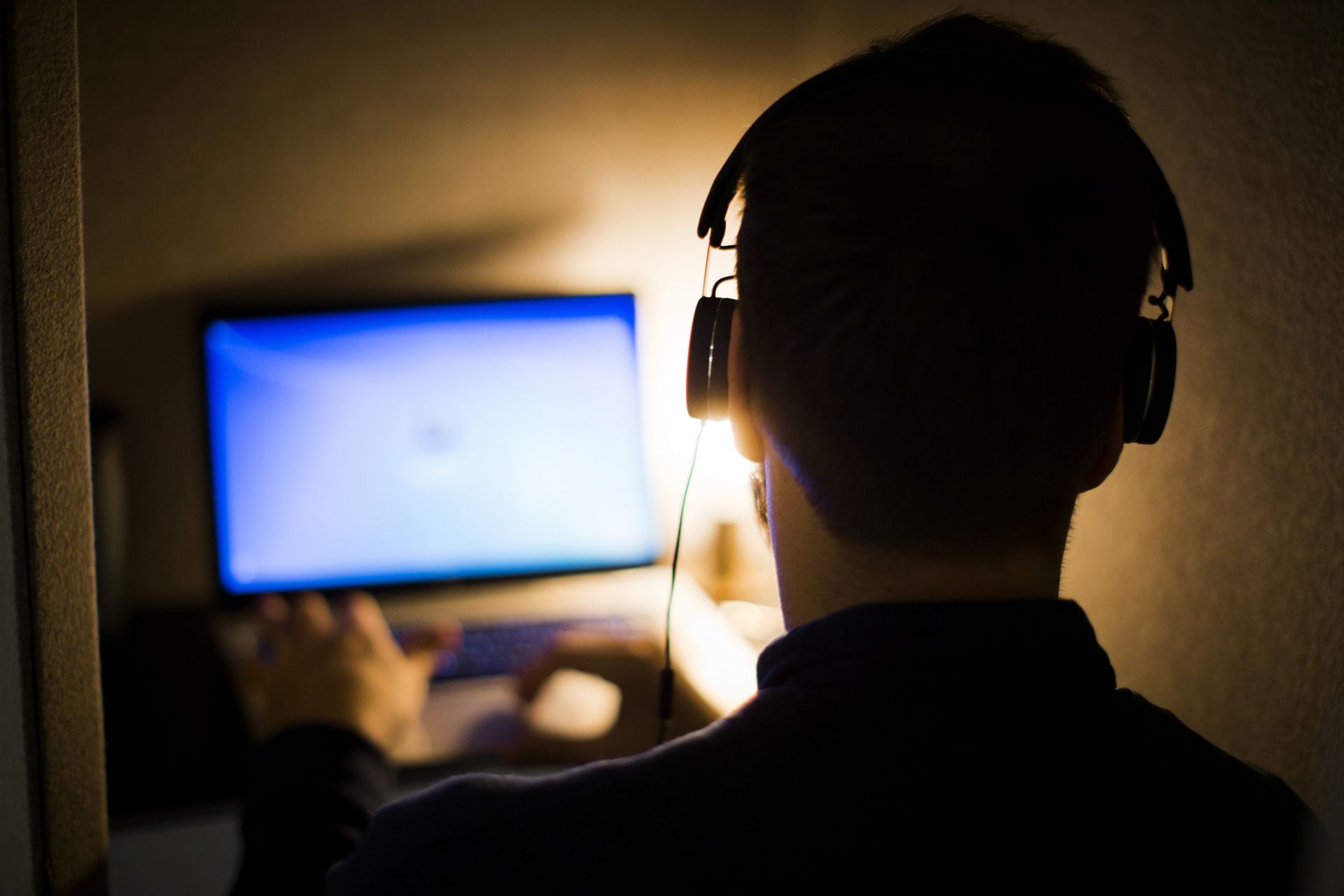 A man with headphones working on computer in the dark. 