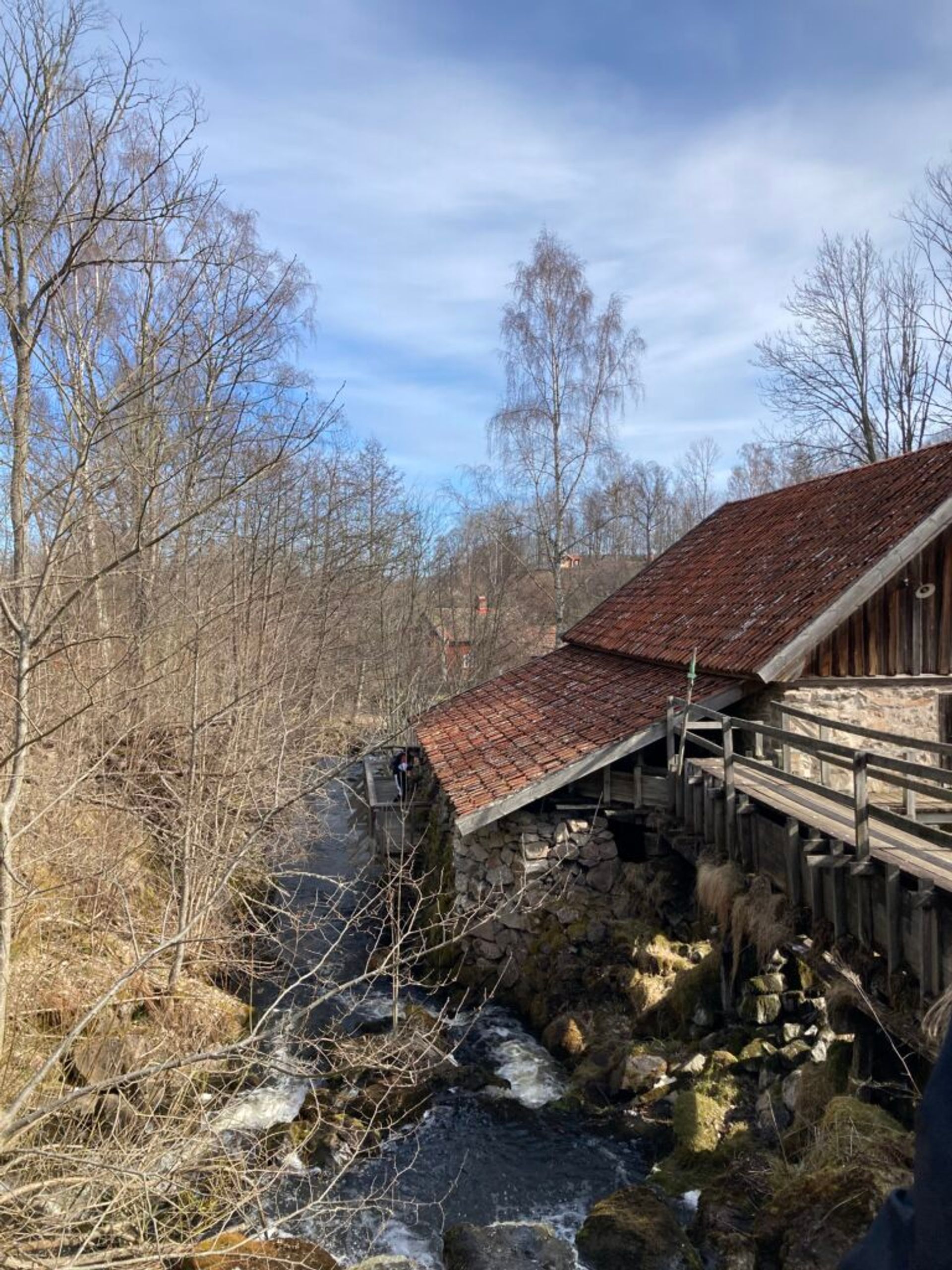 A mill set against a backdrop of bare trees and a flowing stream.