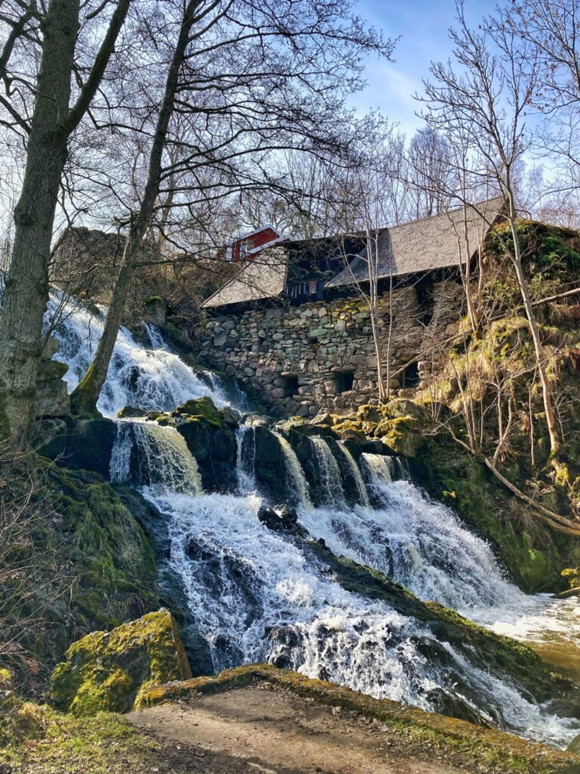 A scenic waterfall cascading beside a rustic stone structure in a natural setting.