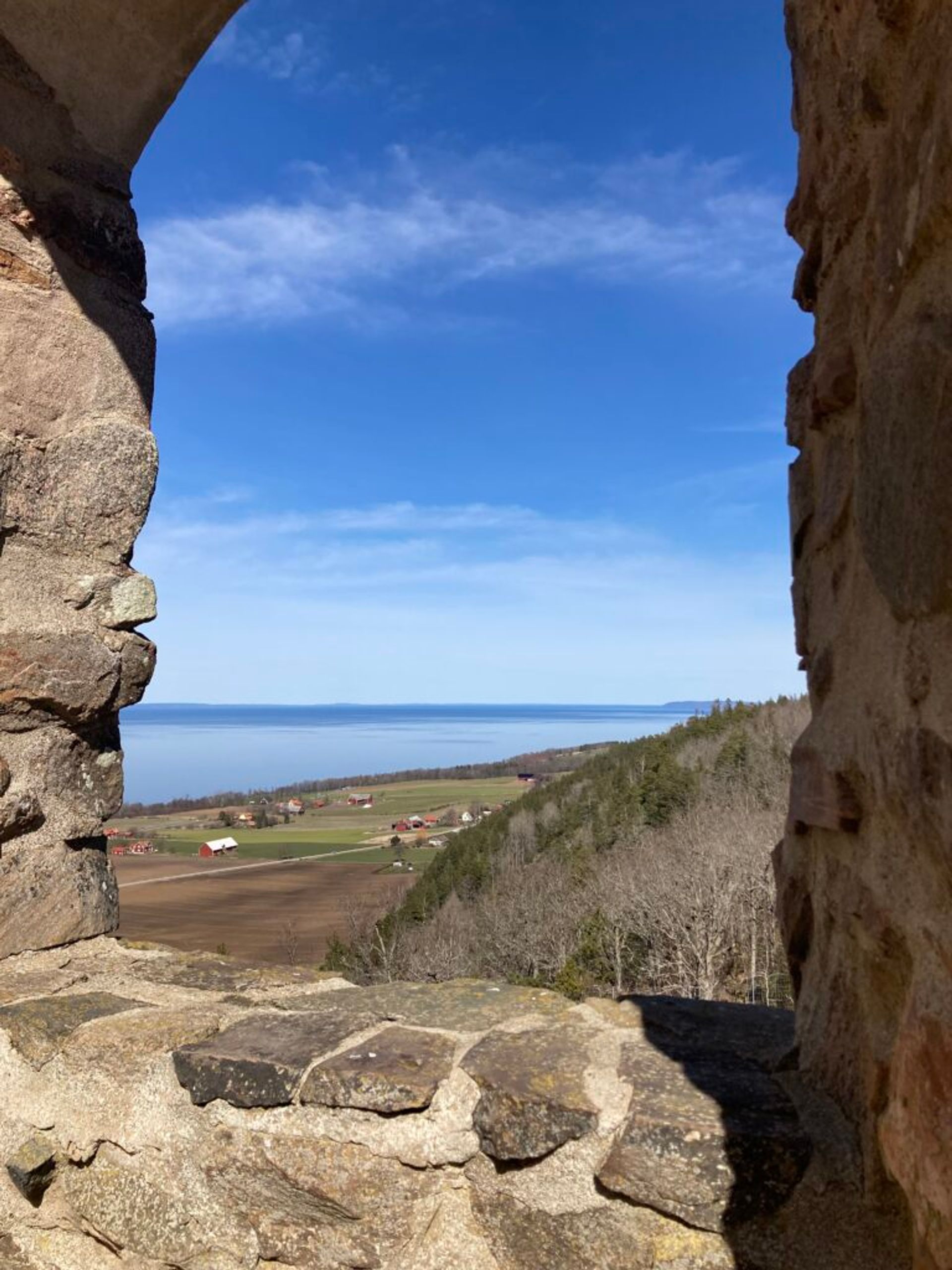 View from castle ruins on a hill, looking out over fields and a lake in the distance.