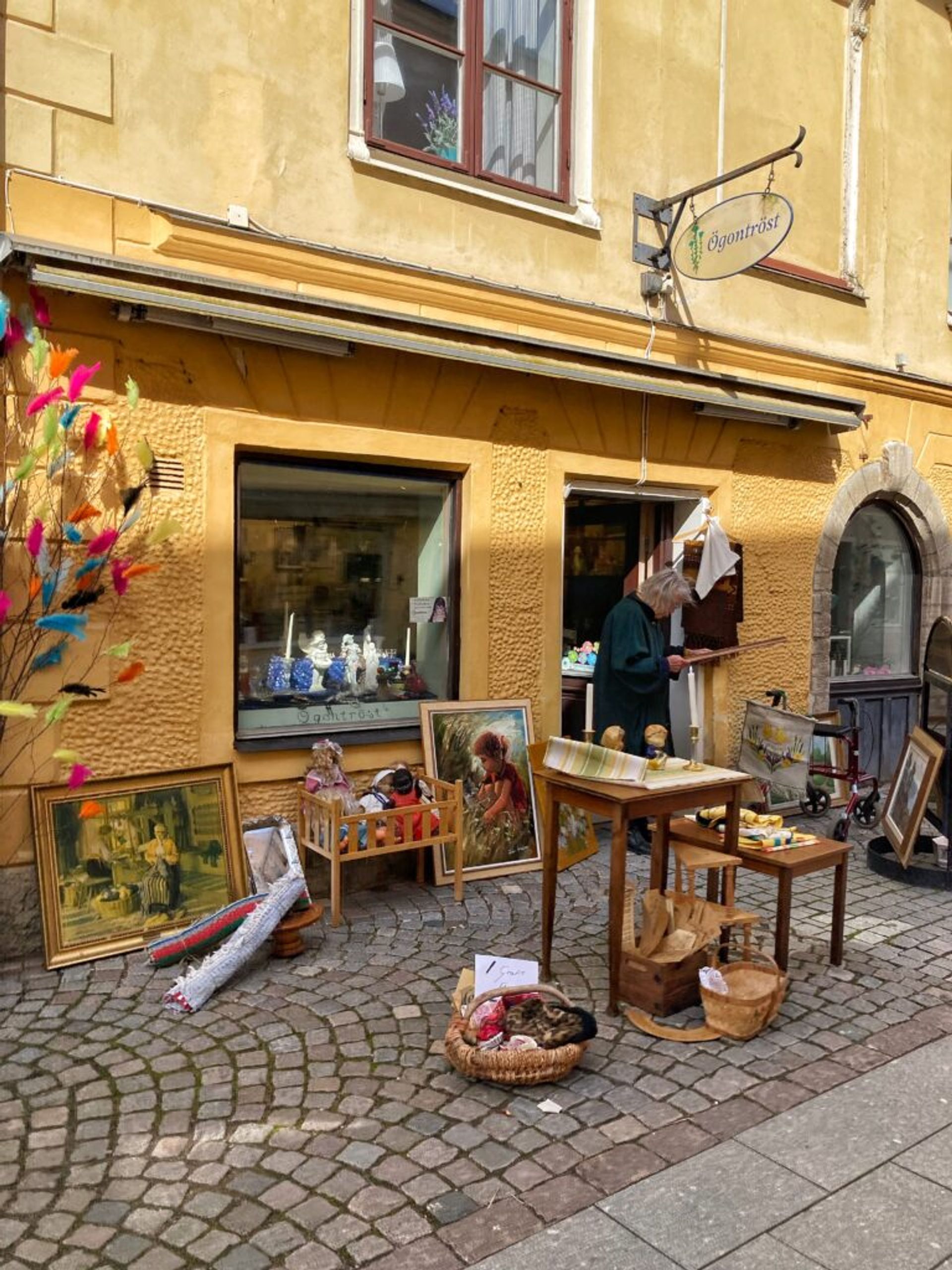 Outdoor art market with paintings for sale by an elderly woman.