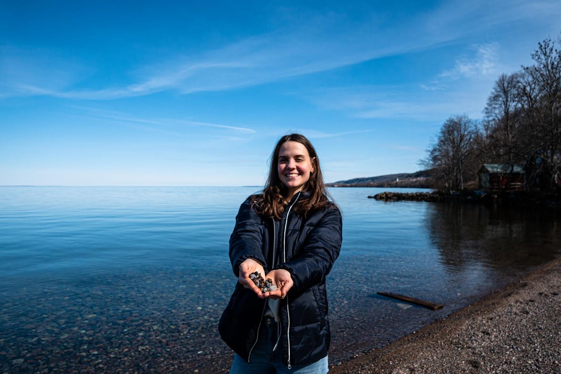 Smiling woman by the beach holding rocks in her hands.