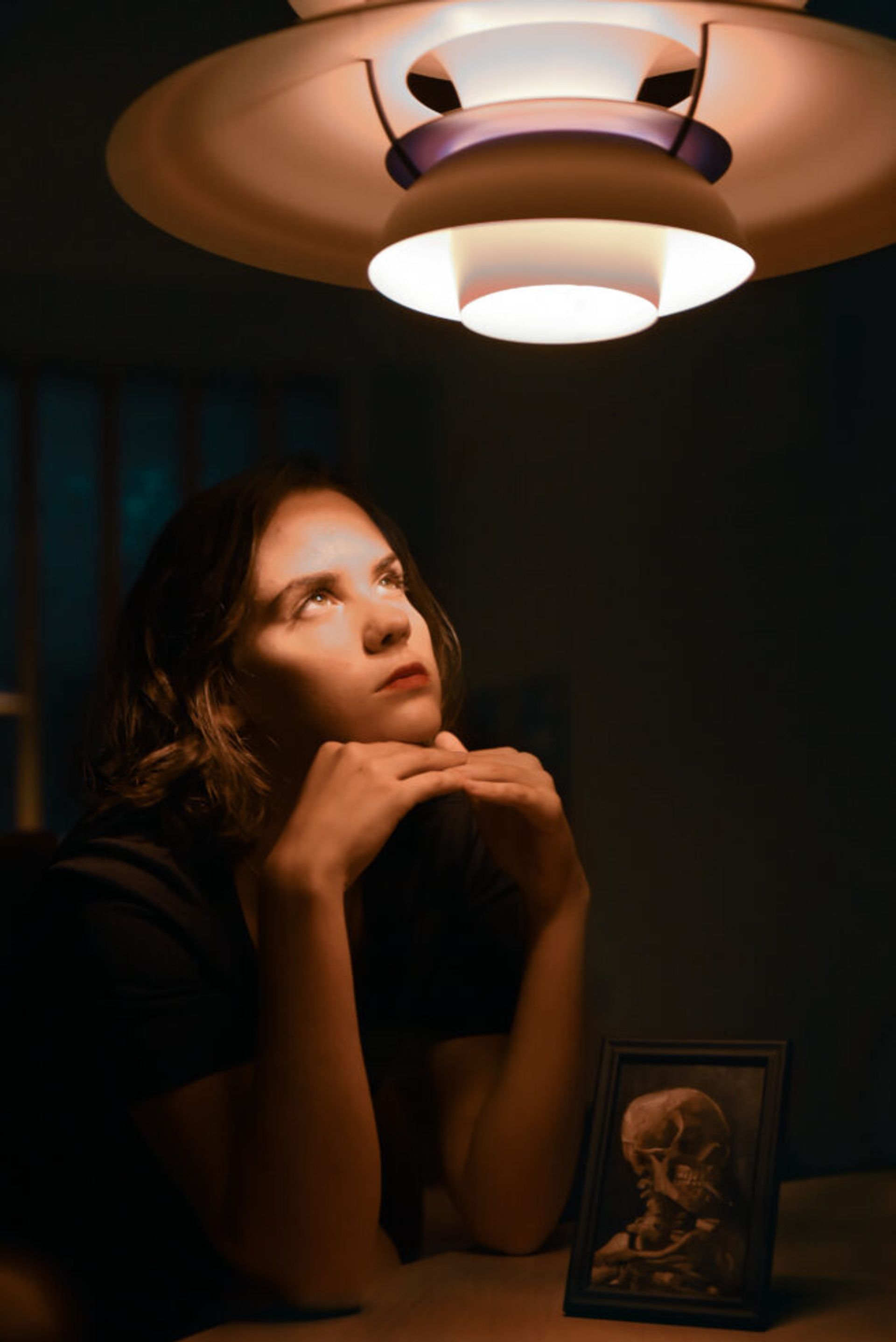 A woman sits beneath a lamp, casting a gentle glow on her face.