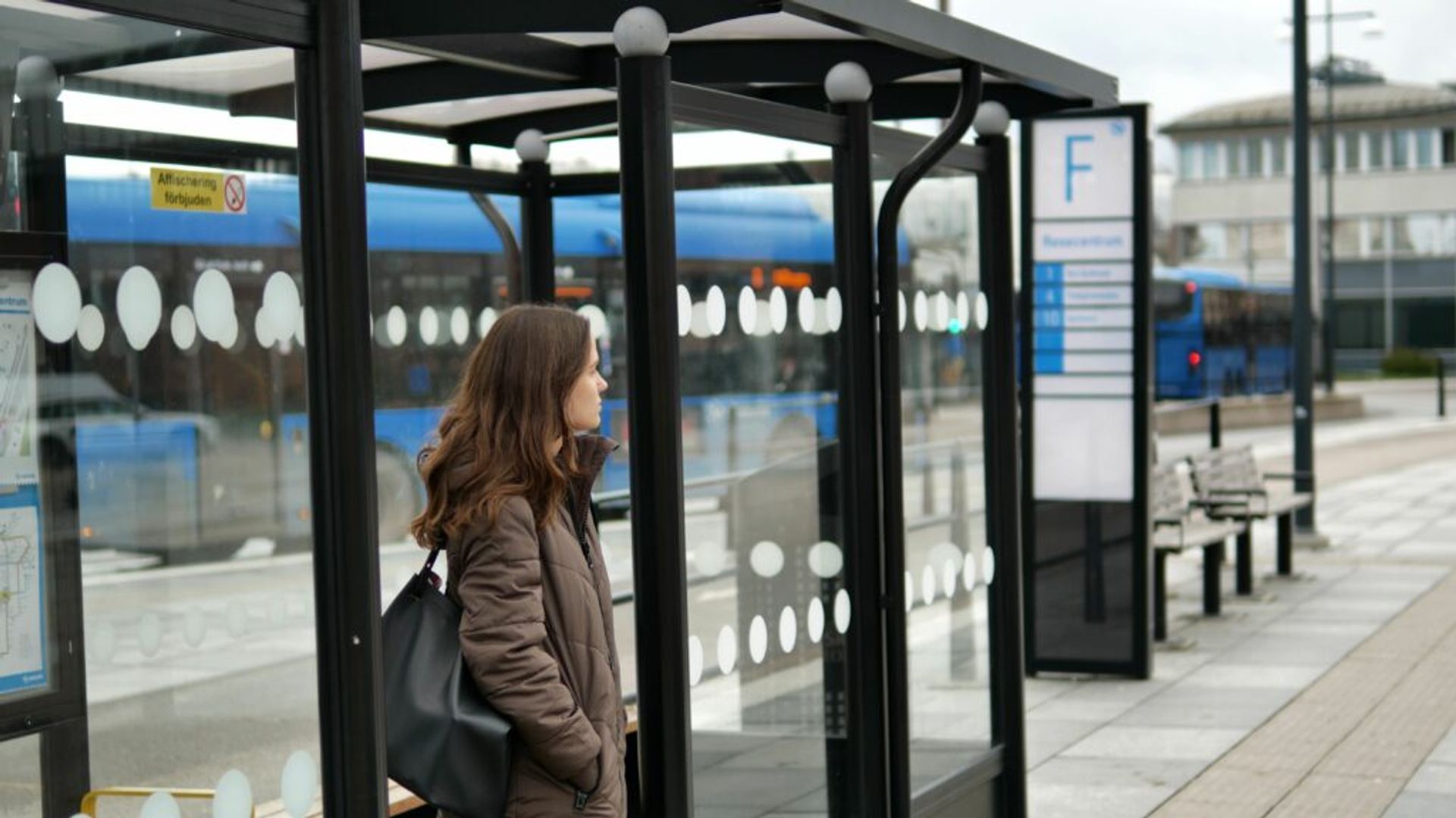 A woman gazes into the distance as she waits at a bus stop.