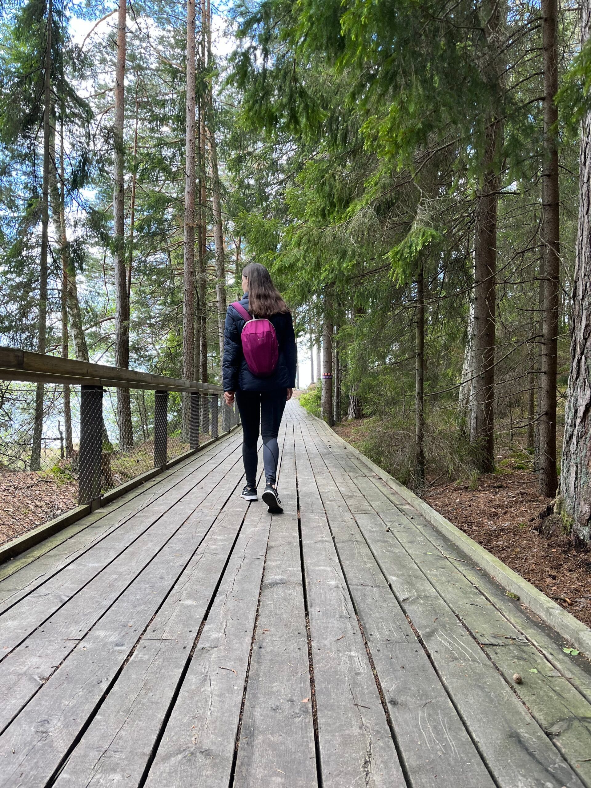 A woman strolls along a wooden bridge in a forest.