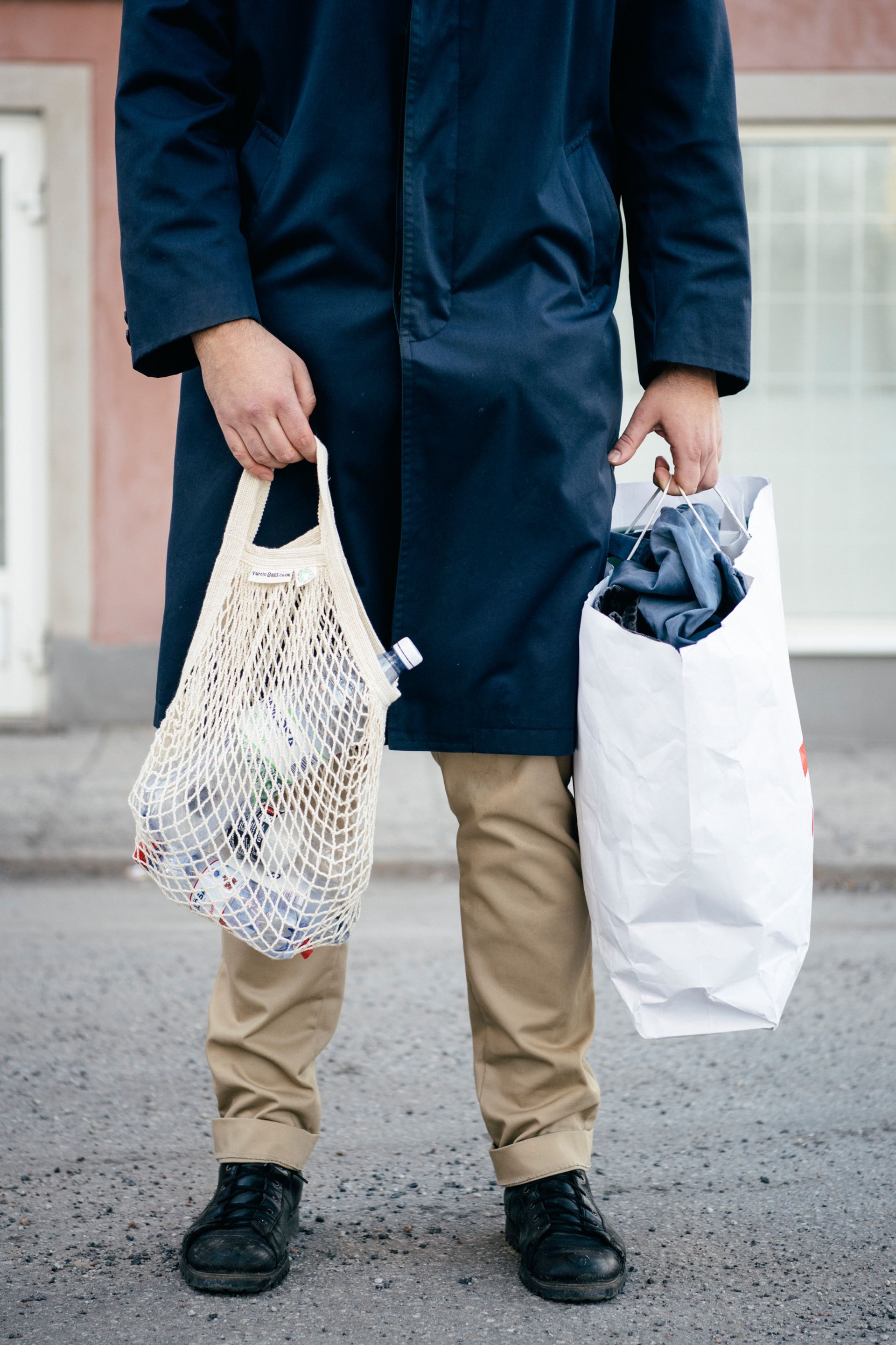 An outdoor lower body shot of a person holding a cloth bag with groceries in one hand and a paper bag in the other.