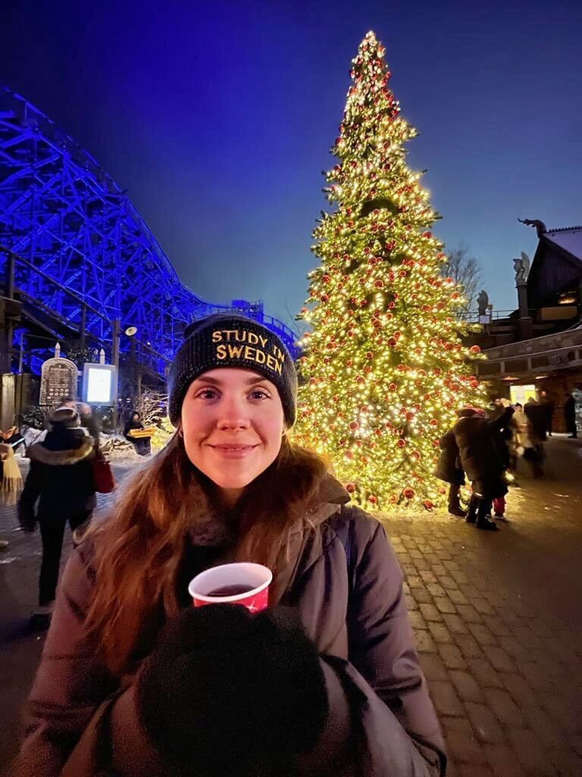A girl posing in front of Christmas tree holding a cup in hands.