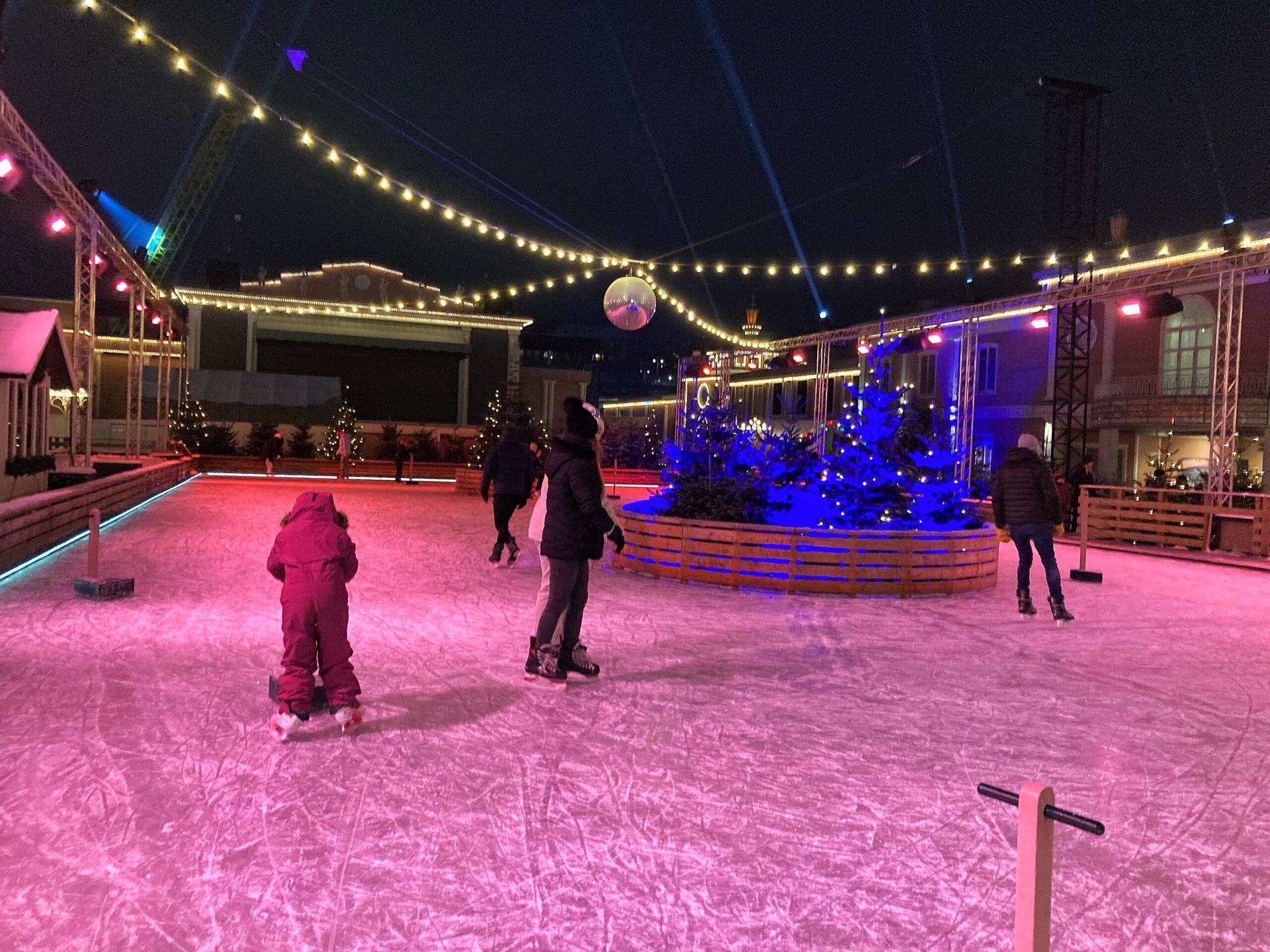 A festive ice-skating rink illuminated by a gentle pink glow.