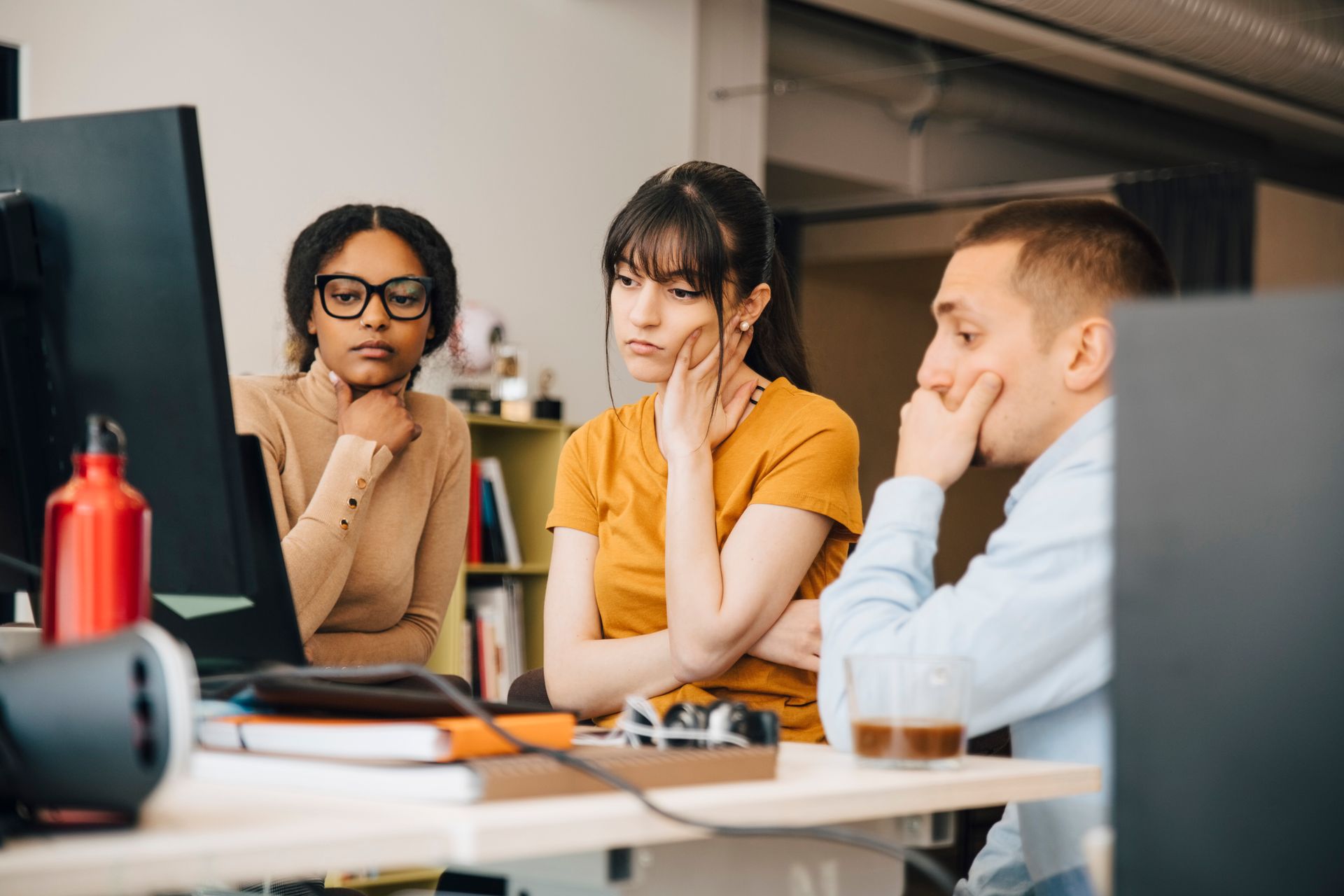 Three people, their expressions pensive, gather around a computer.