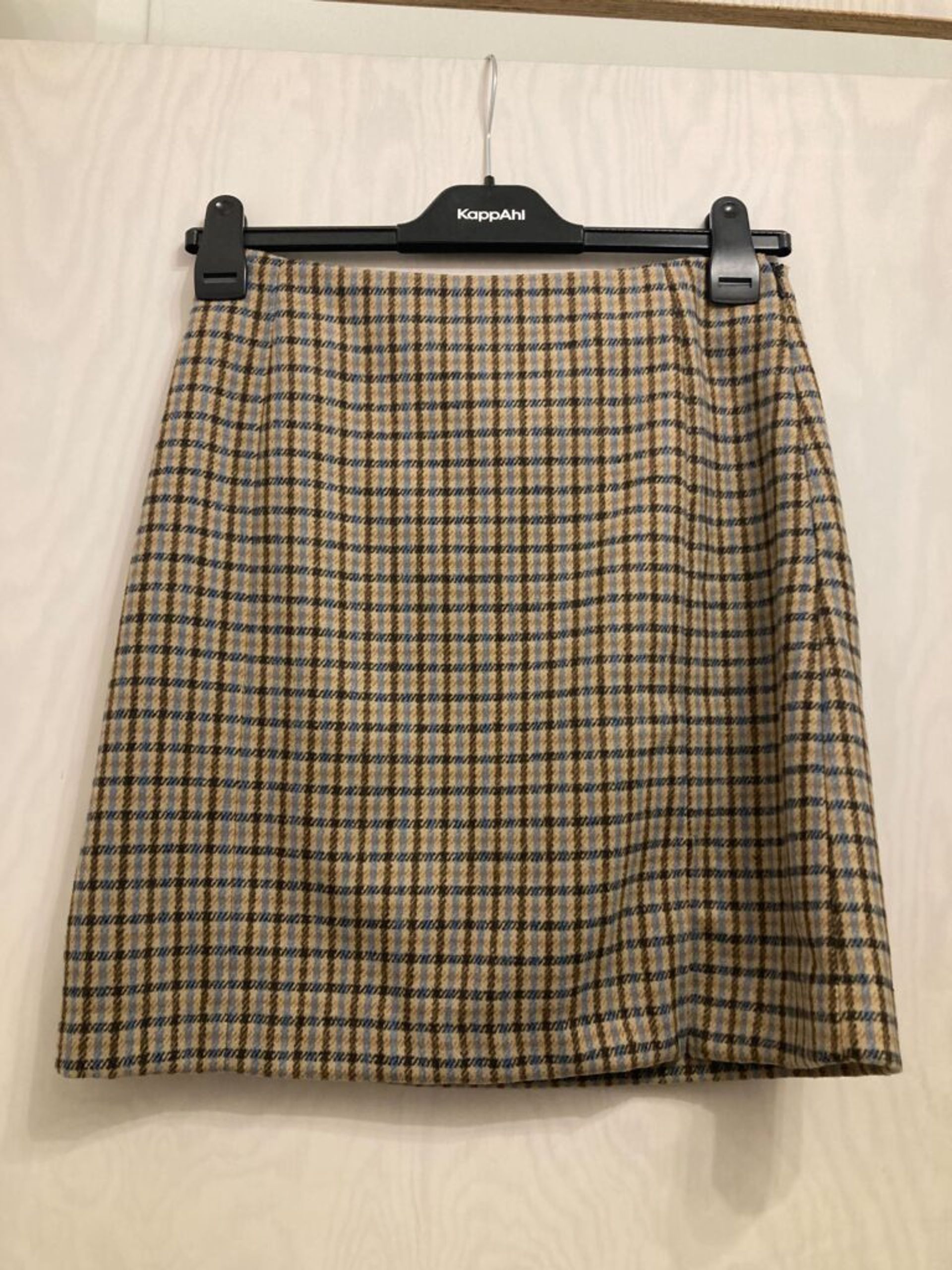 A beige plaid skirt on a clothing hanger.