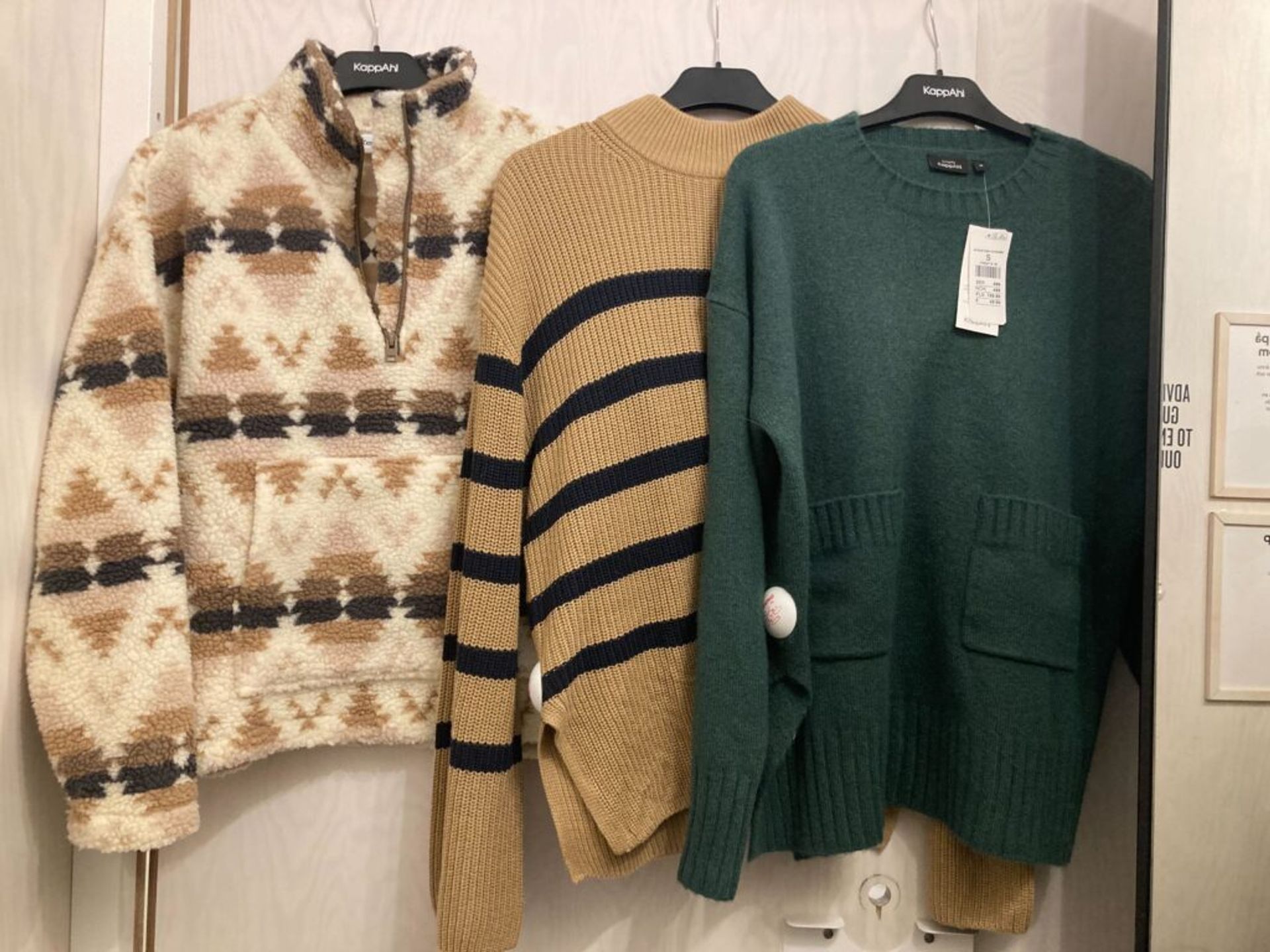 Sweaters in an array of colors and patterns hanging in a changing room.