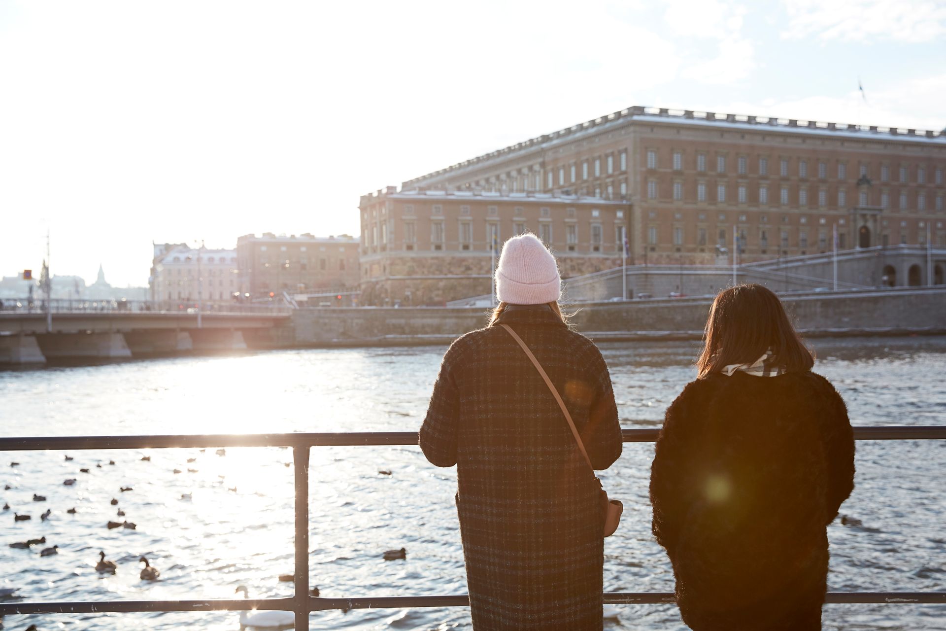 Two people looking at the Royal Palace in Stockholm from across a river.