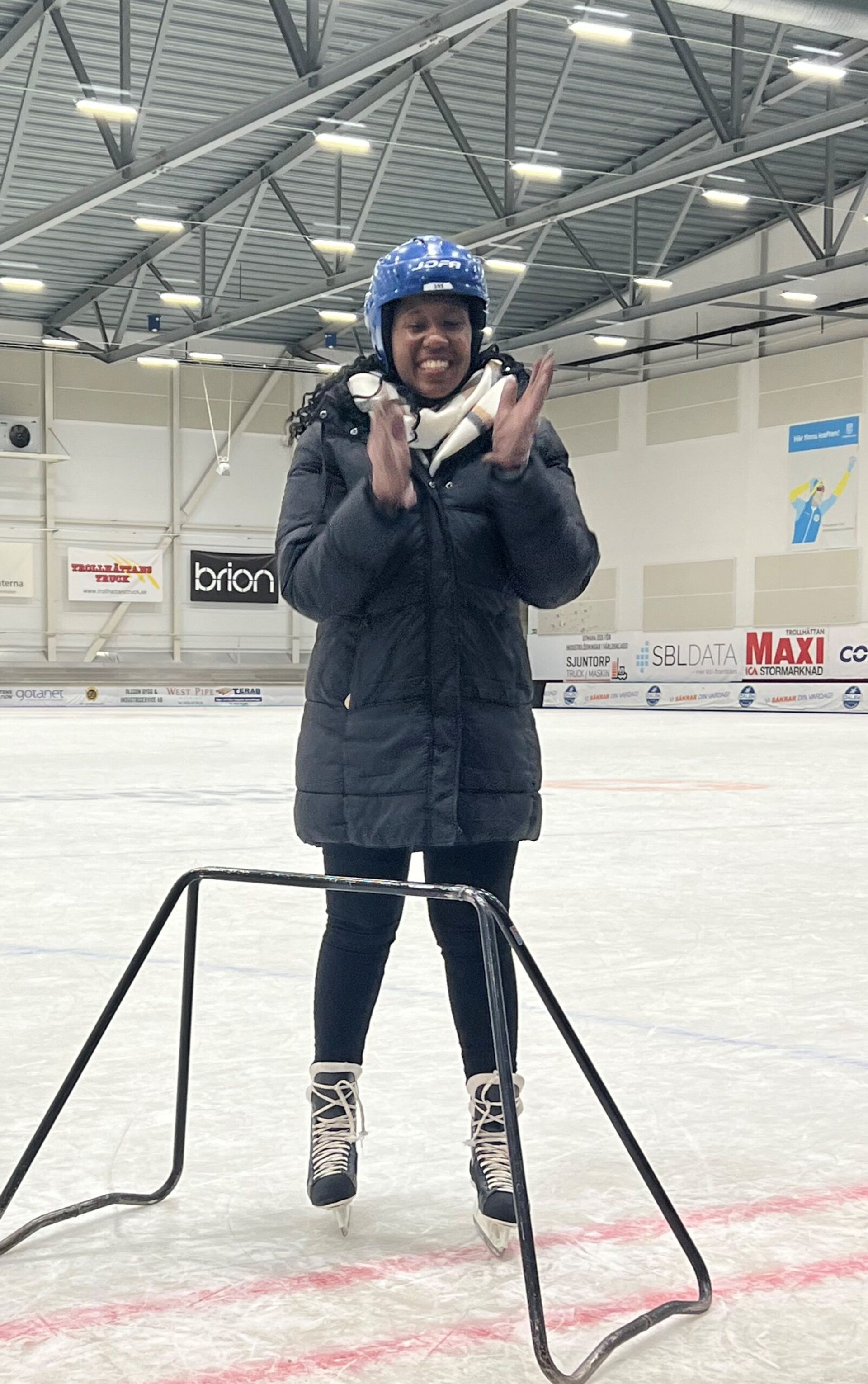 A woman wearing ice skates stands on an indoor ice skating rink.