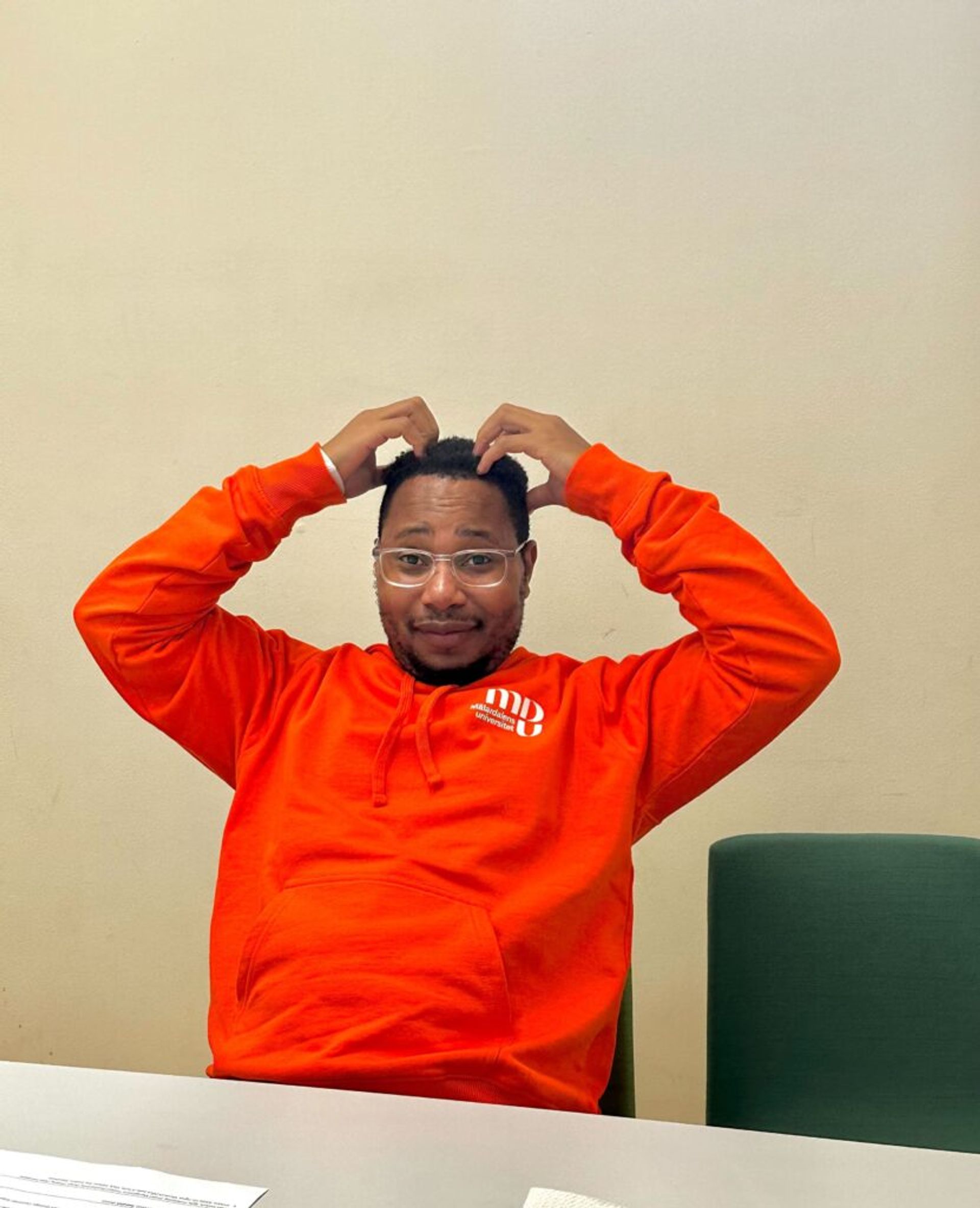 A person wearing an orange hoodie looks puzzled as they scratch their head.