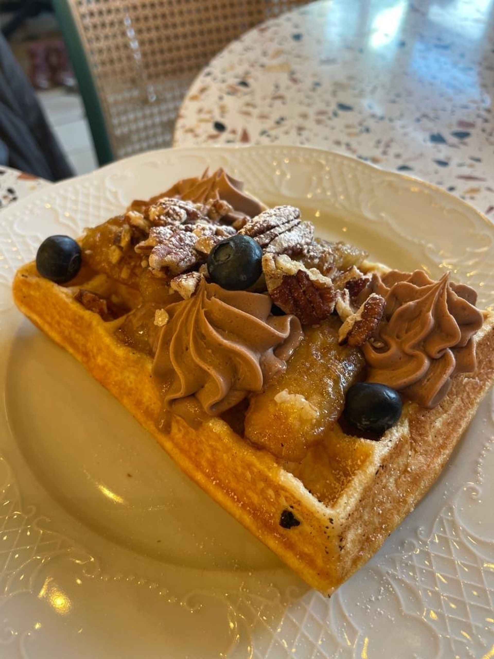 A close-up of a waffle with blueberries, jam, and walnuts.