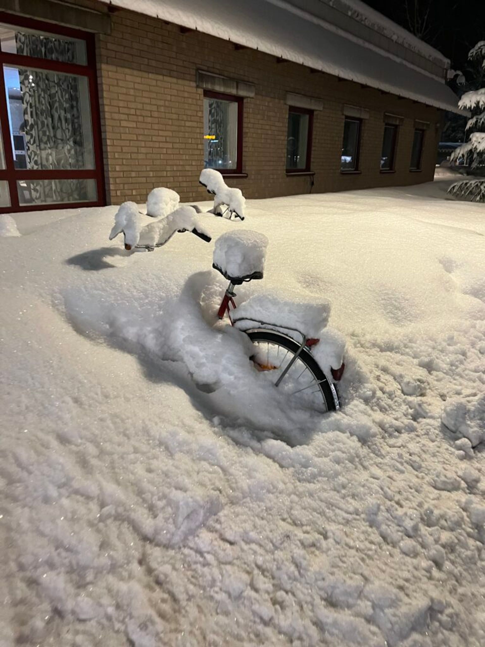 Snow-covered bikes parked beside a building.