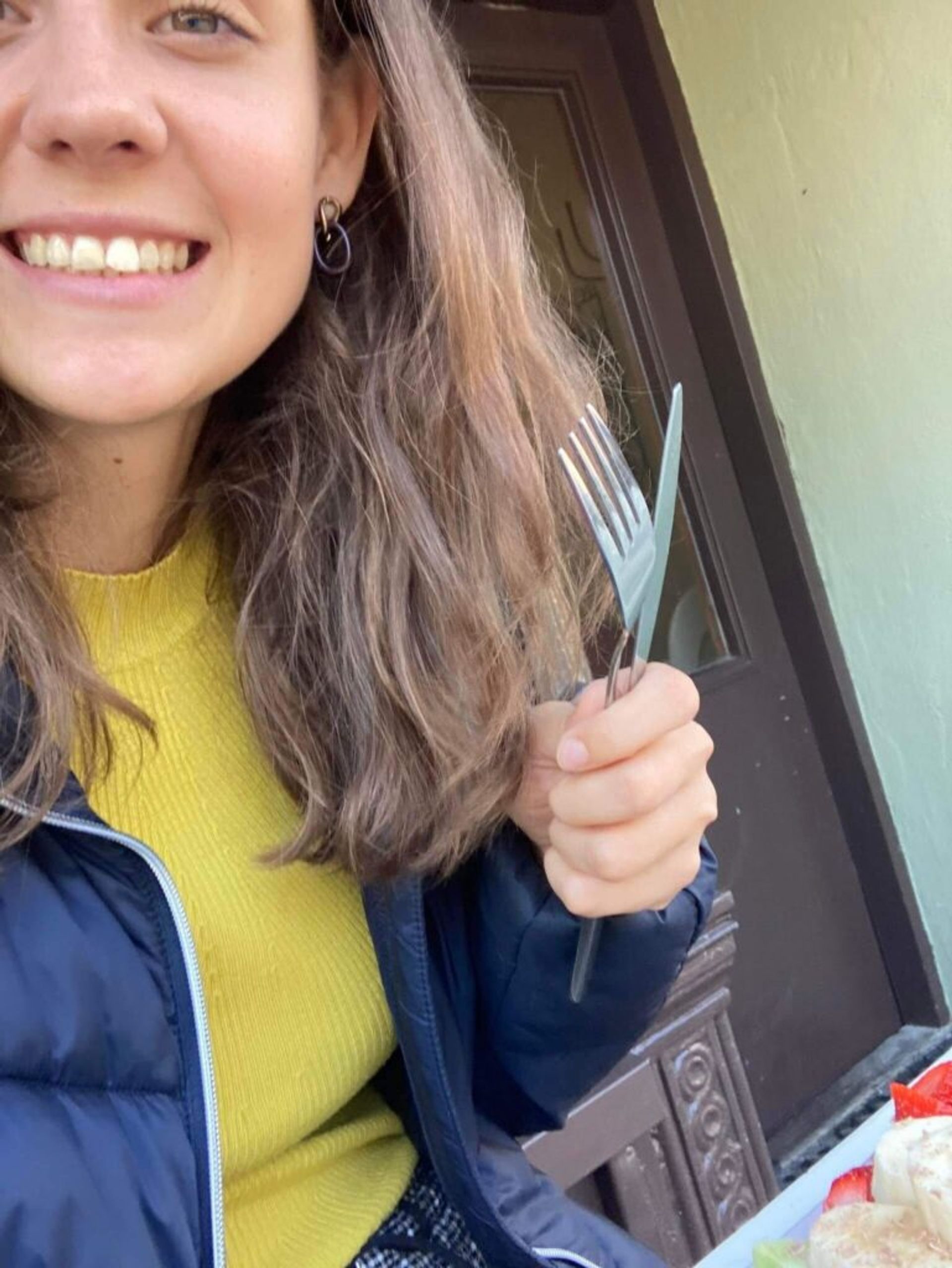 A cheerful selfie of a woman holding a fork and knife, ready to enjoy waffles.