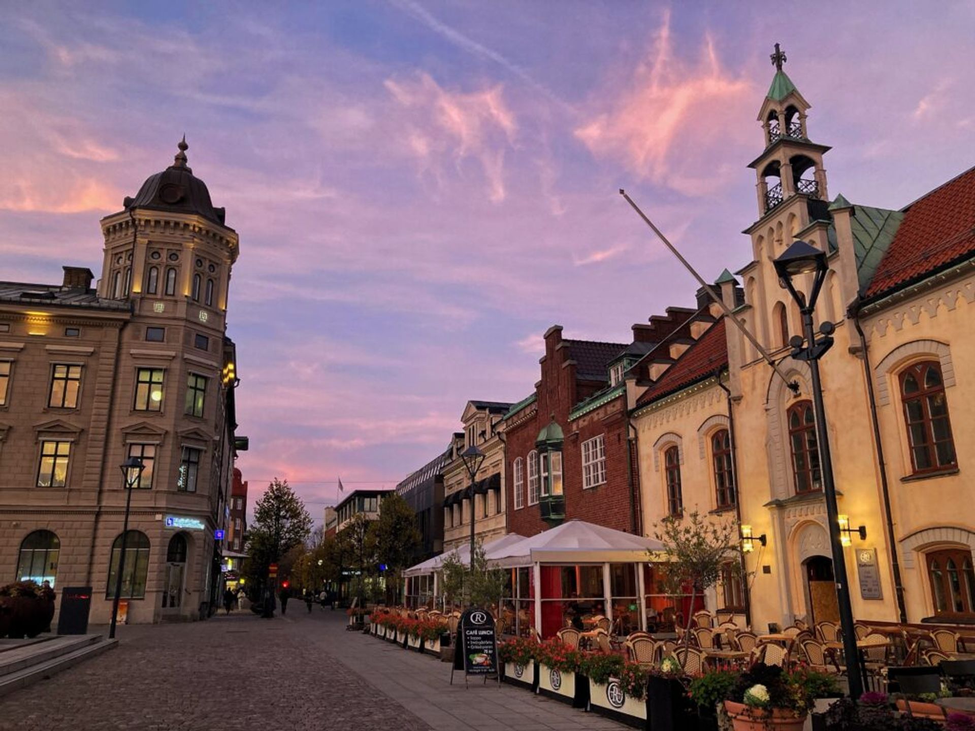 A cobblestone street flanked by historical buildings, featuring a café with outdoor seating.