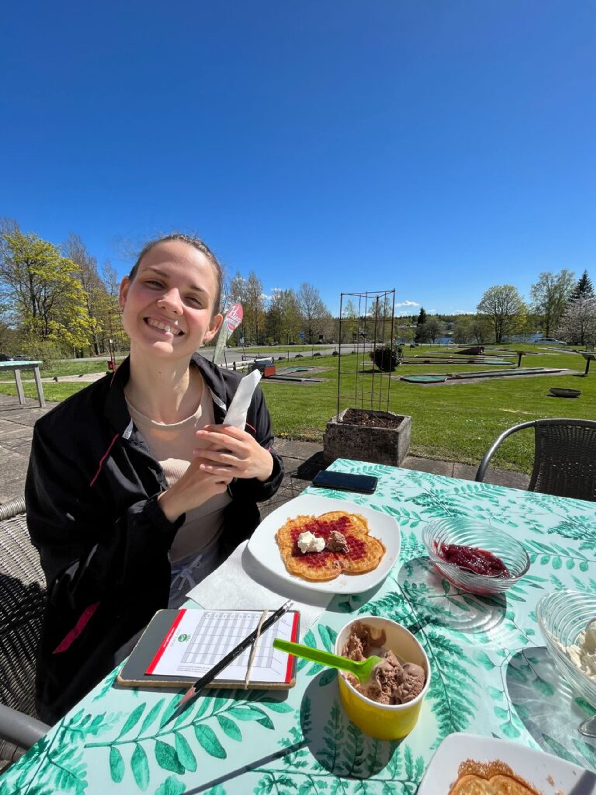 A smiling woman enjoys waffles at an outdoor table.