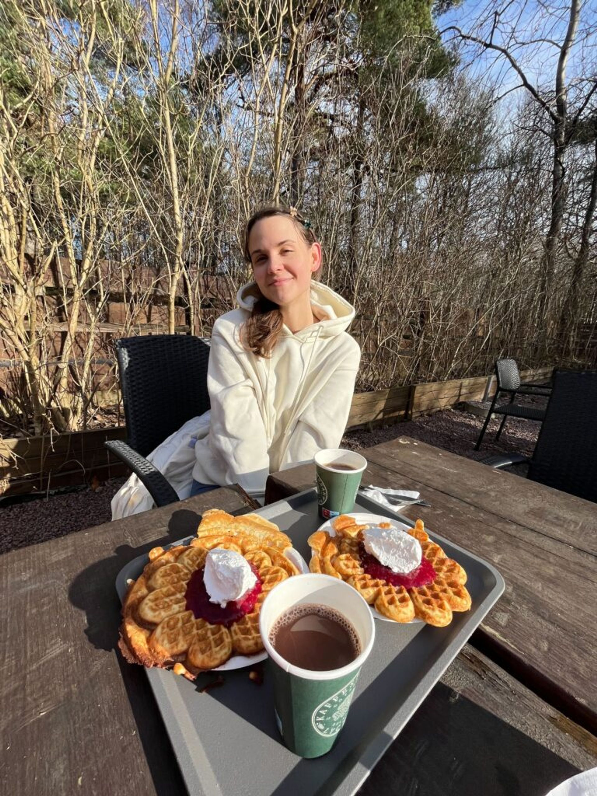 A woman poses at a table set with waffles and hot beverages.