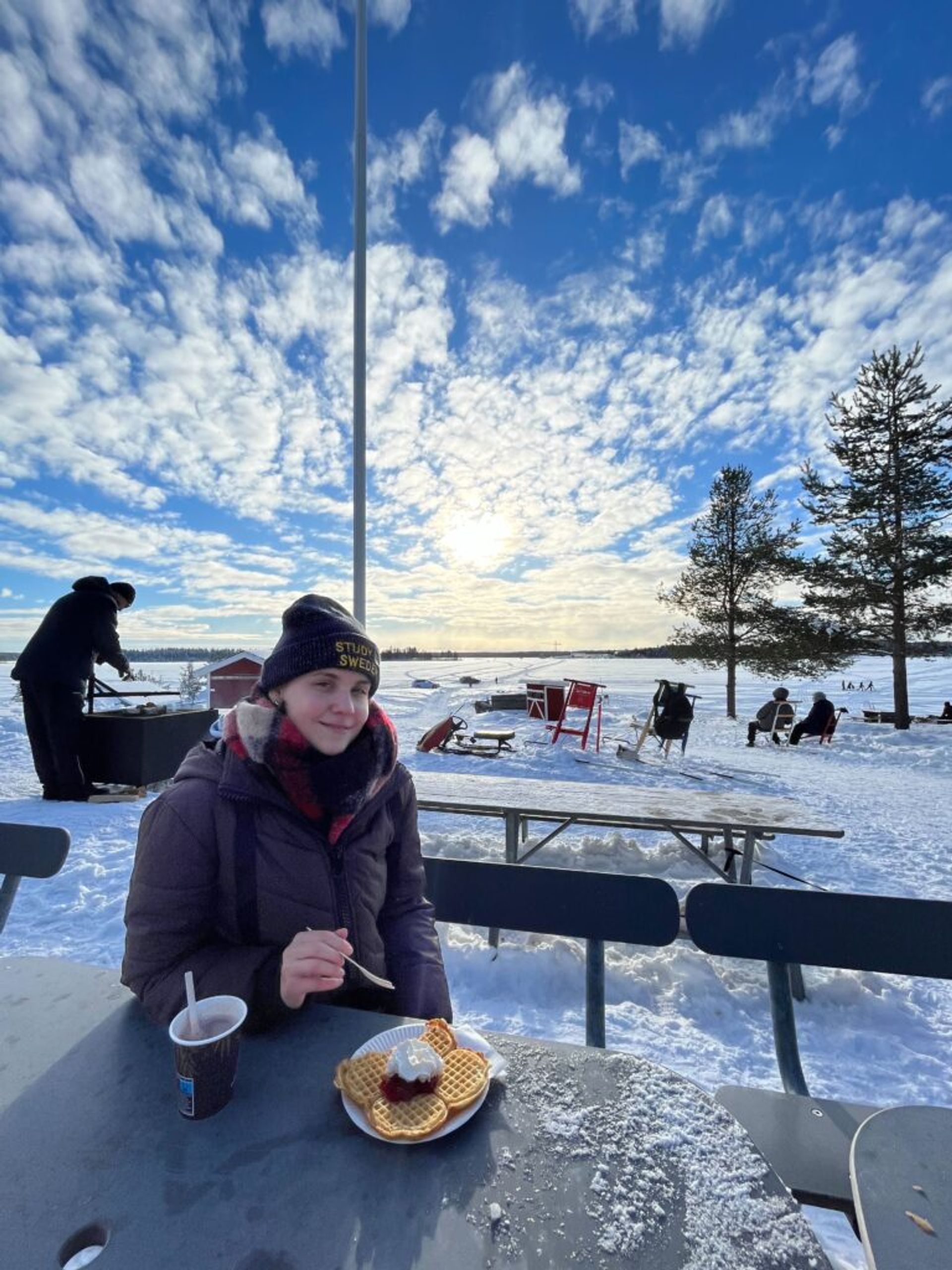 A woman enjoys waffles at an outdoor picnic table during winter.