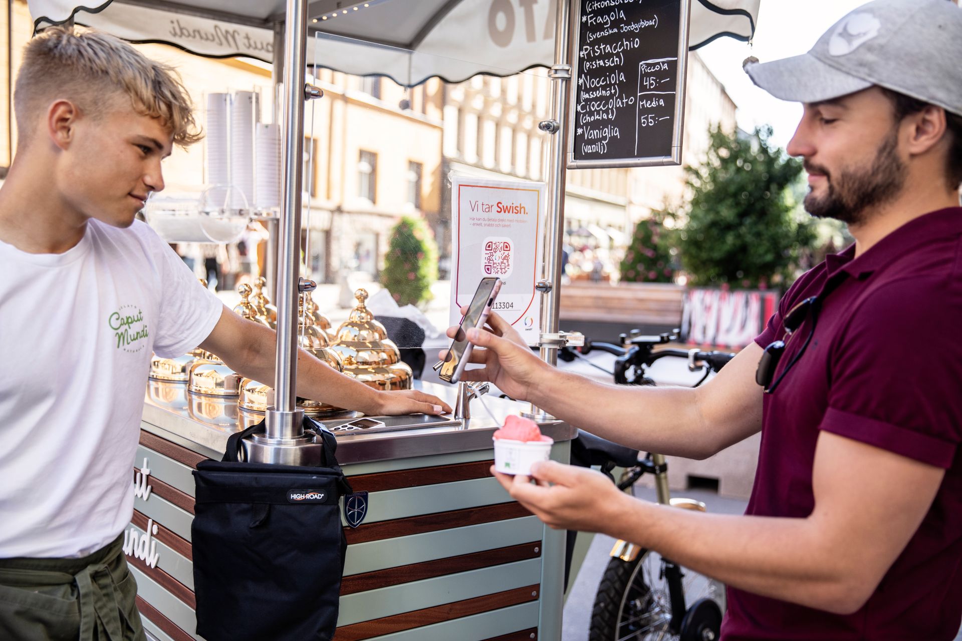 Using his smartphone, a young man purchases an ice cream from a stand.