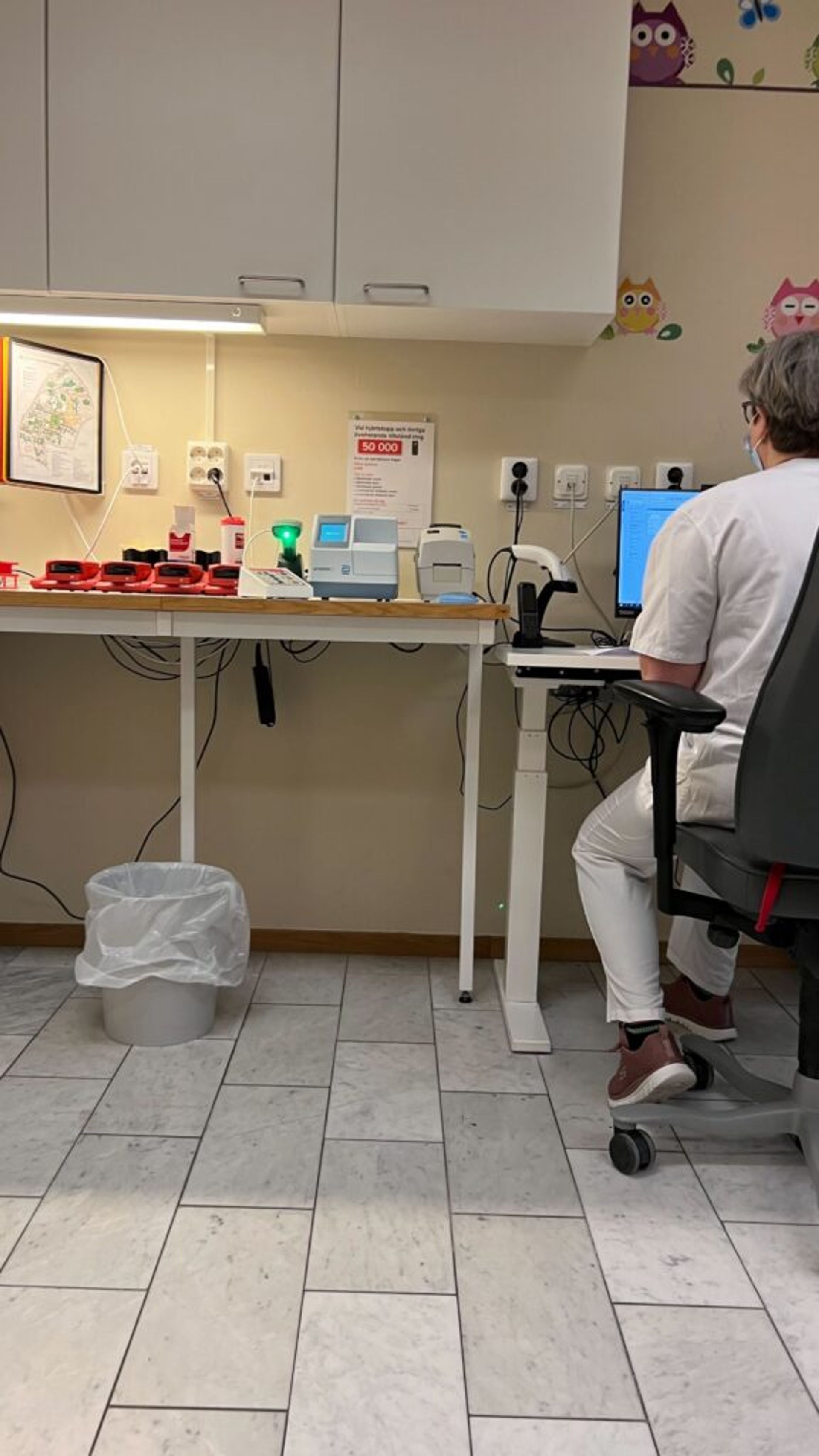 A healthcare professional is seated at a desk, surrounded by medical equipment.