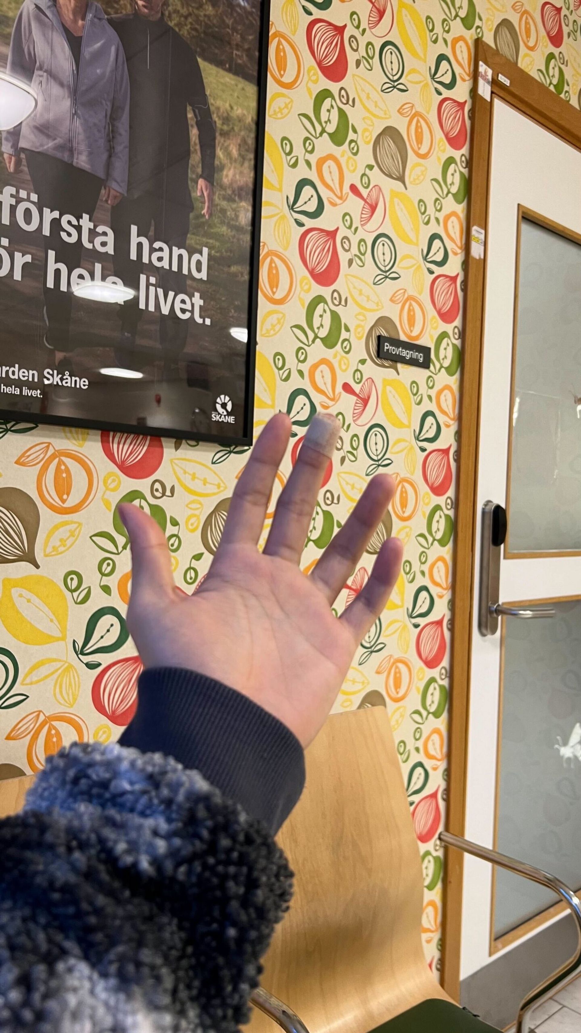 A close-up of a hand with a band-aid, set against the backdrop of a doctor's waiting room.