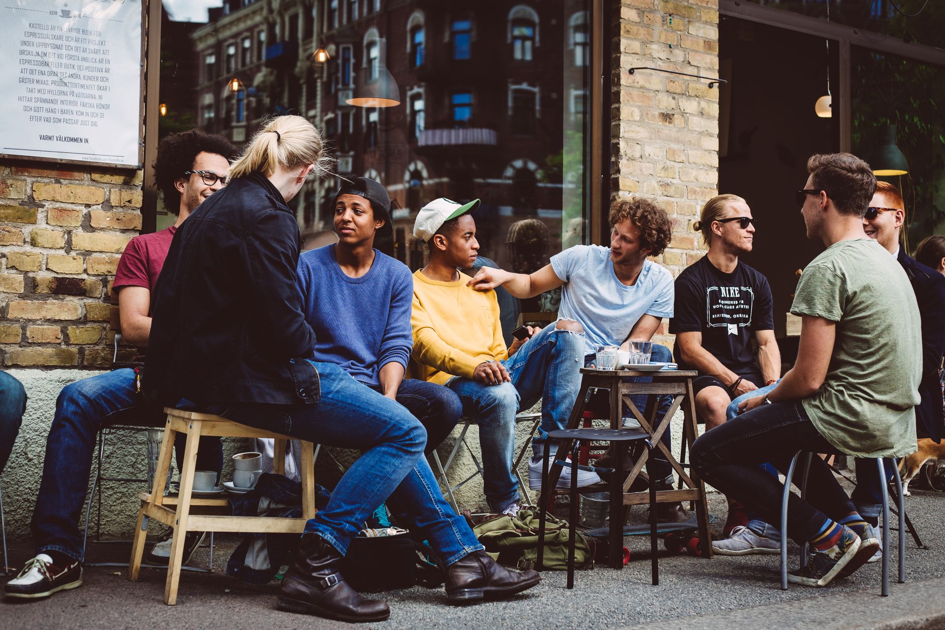 A group of people engaged in conversation, seated in the outdoor section of a café.